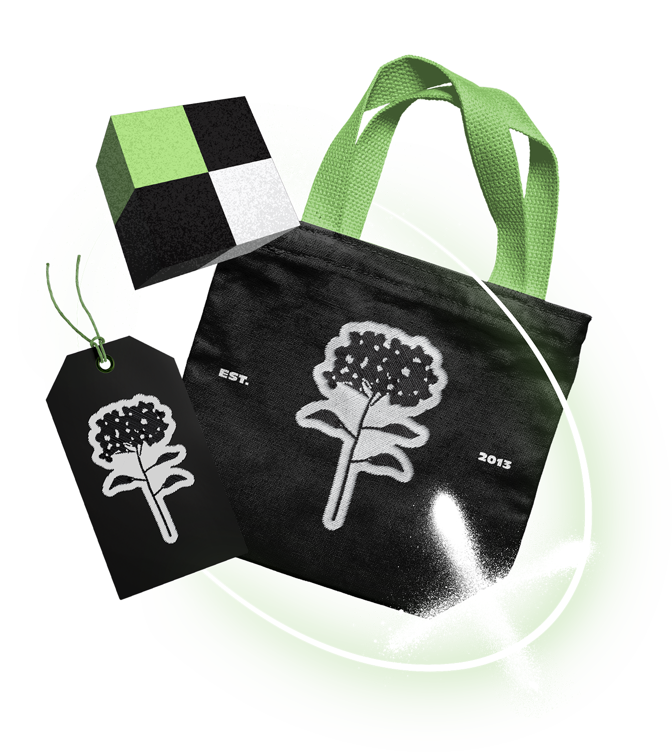 A black tote bag and a matching luggage tag both featuring a white hydrangea logo symbol, with the text "EST. 2013" on the bag. A cube-shaped object with a black, white, and green checkered pattern is also present.