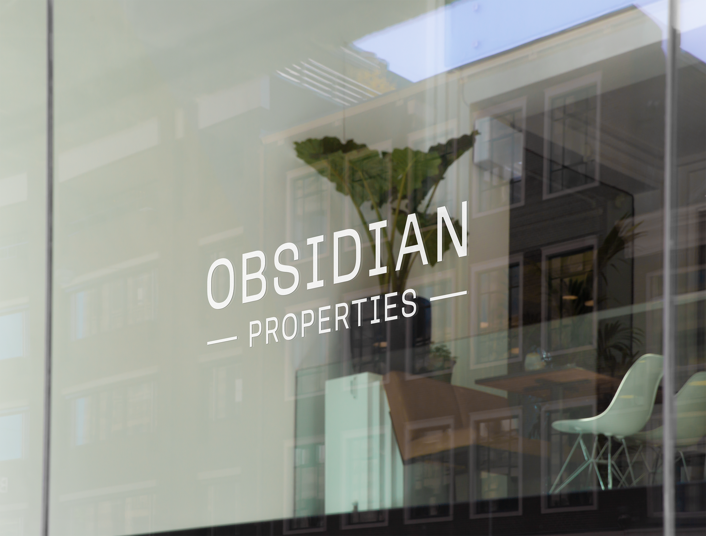 Glass store-front of a store with the white all-text logo on the window reading "Obsidian Properties" in front of a modern interior.