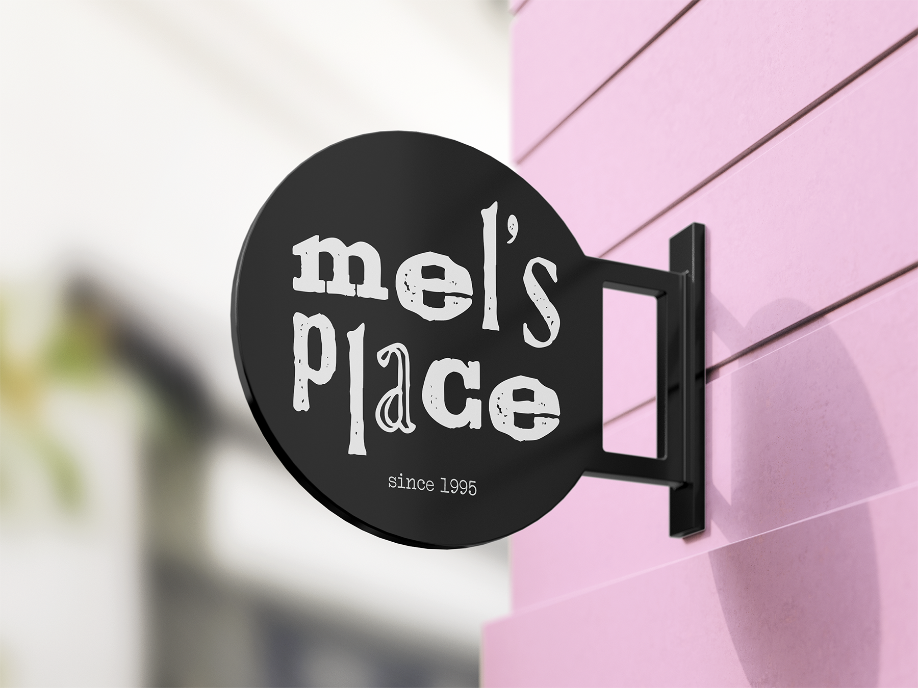 A black circular sign with white text reading 'melo's place since 1995' attached to a pink wall.