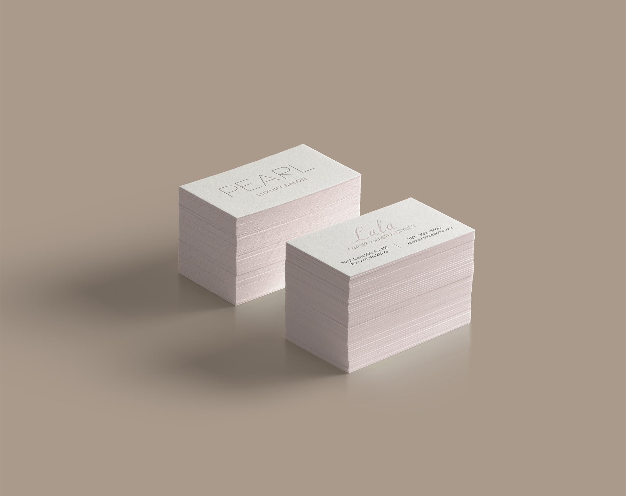 Stacks of cream-colored business cards with pastel pink and tan text, advertising a luxury salon. The cards are on a neutral beige surface with a plain background.