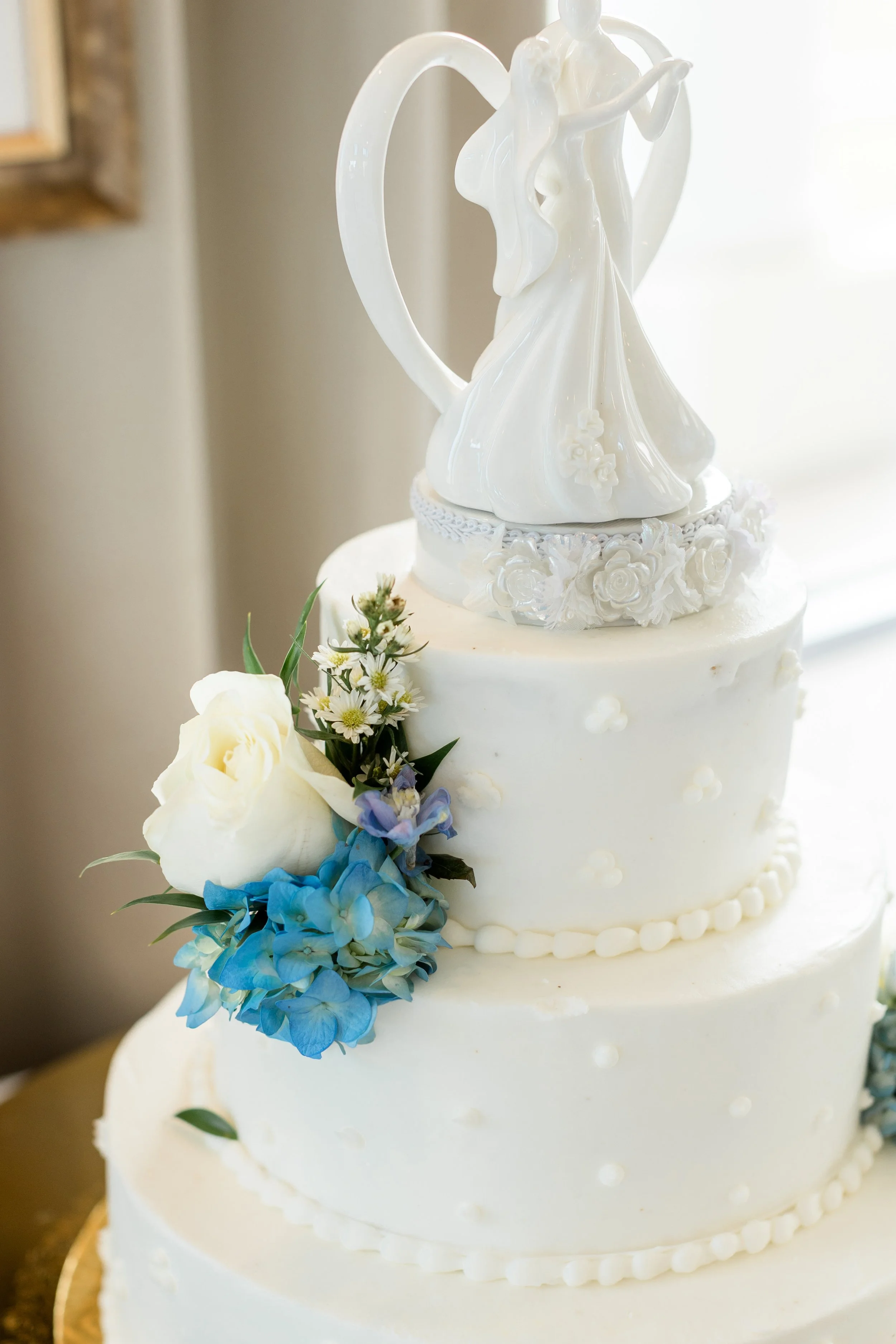 White wedding cake with floral decorations and a bridal figurine on top.