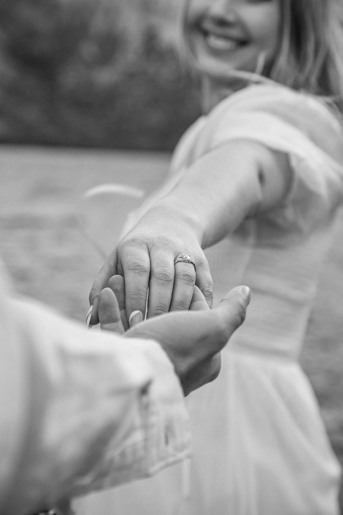 black and white photo of man holding smiling woman's hand with engagement ring