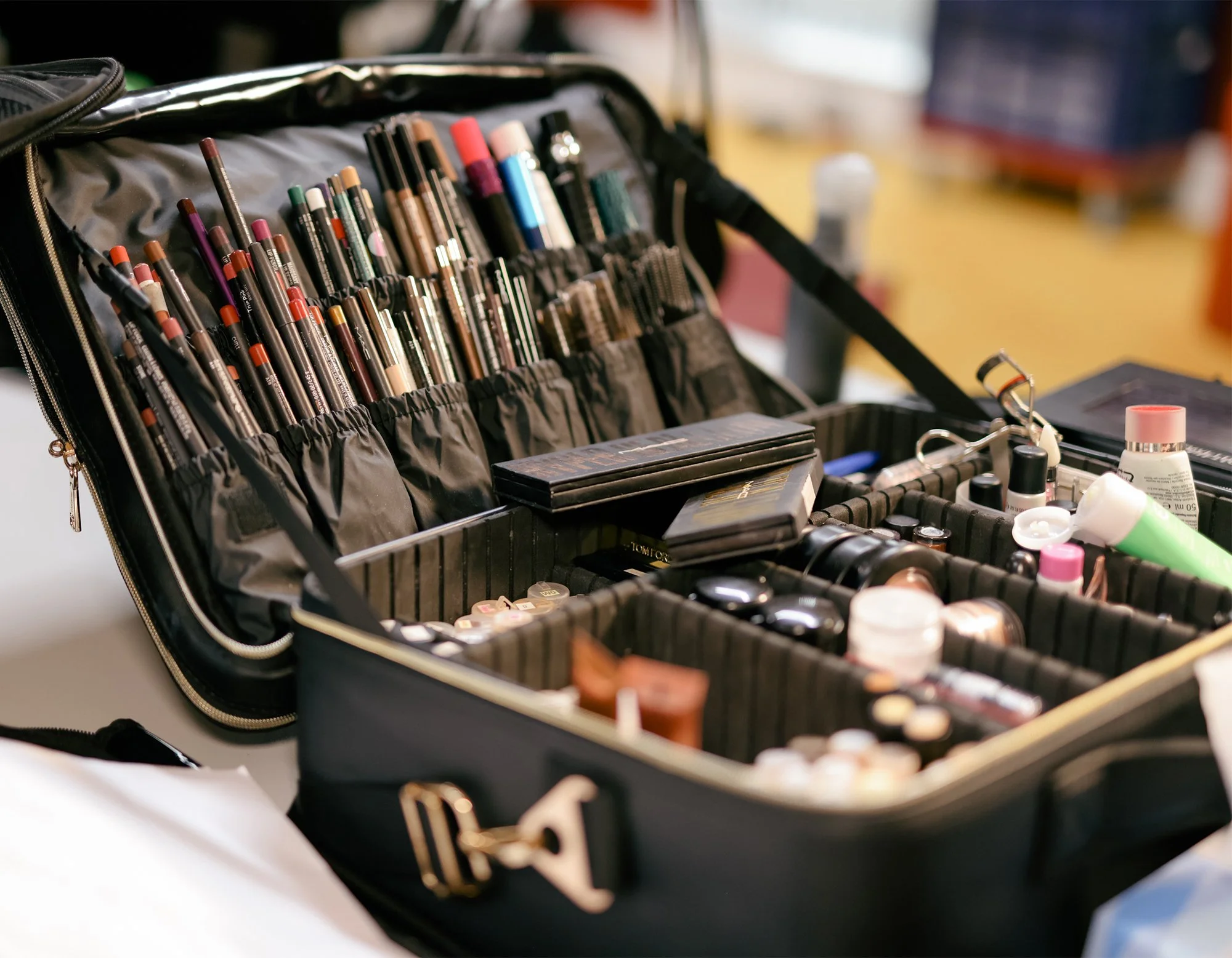 A black makeup case open, filled with various makeup brushes, lipsticks, and skincare products on a white surface.
