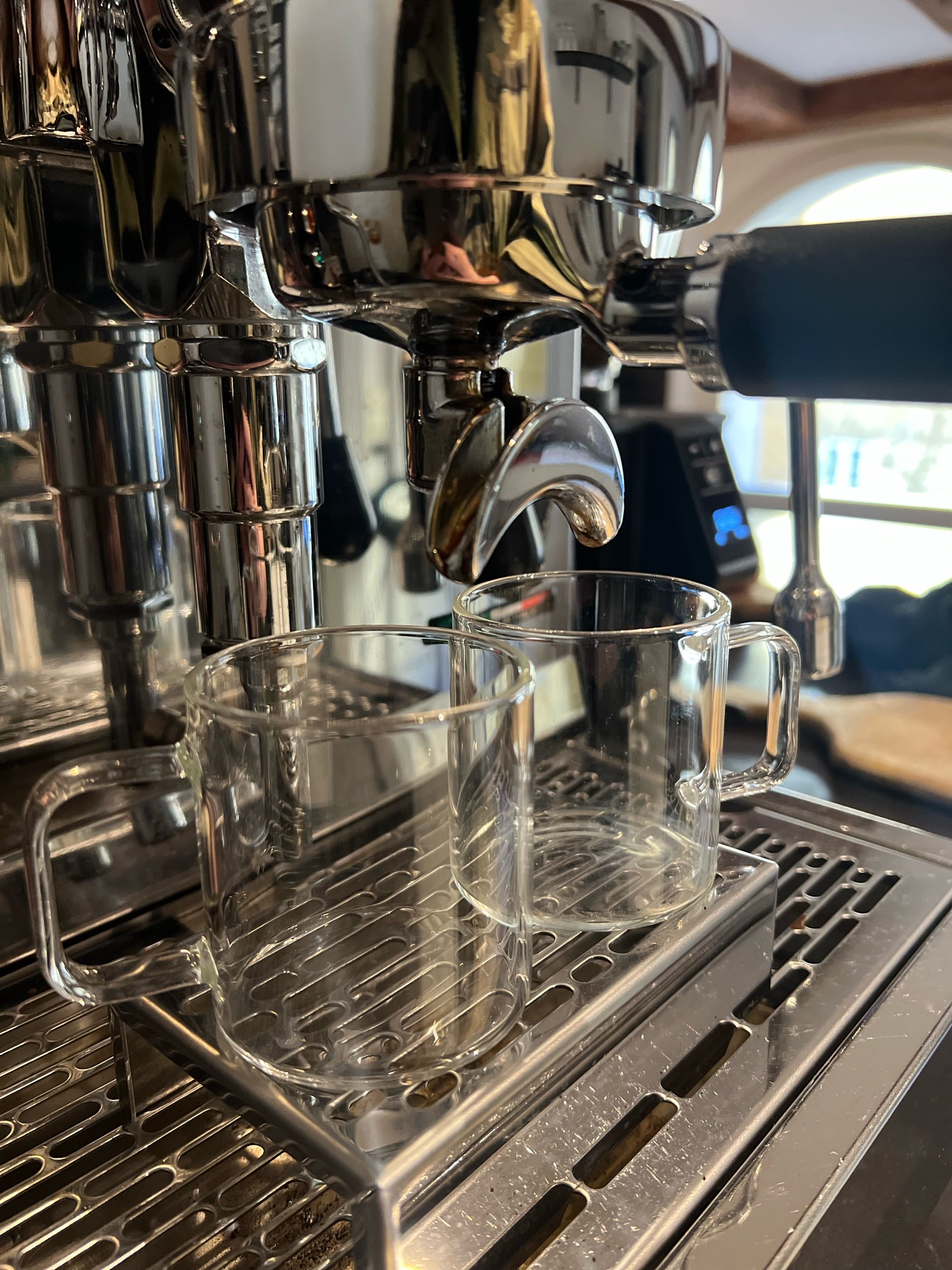 Close-up of a professional espresso machine brewing espresso into glass mugs on a stainless steel drip tray.