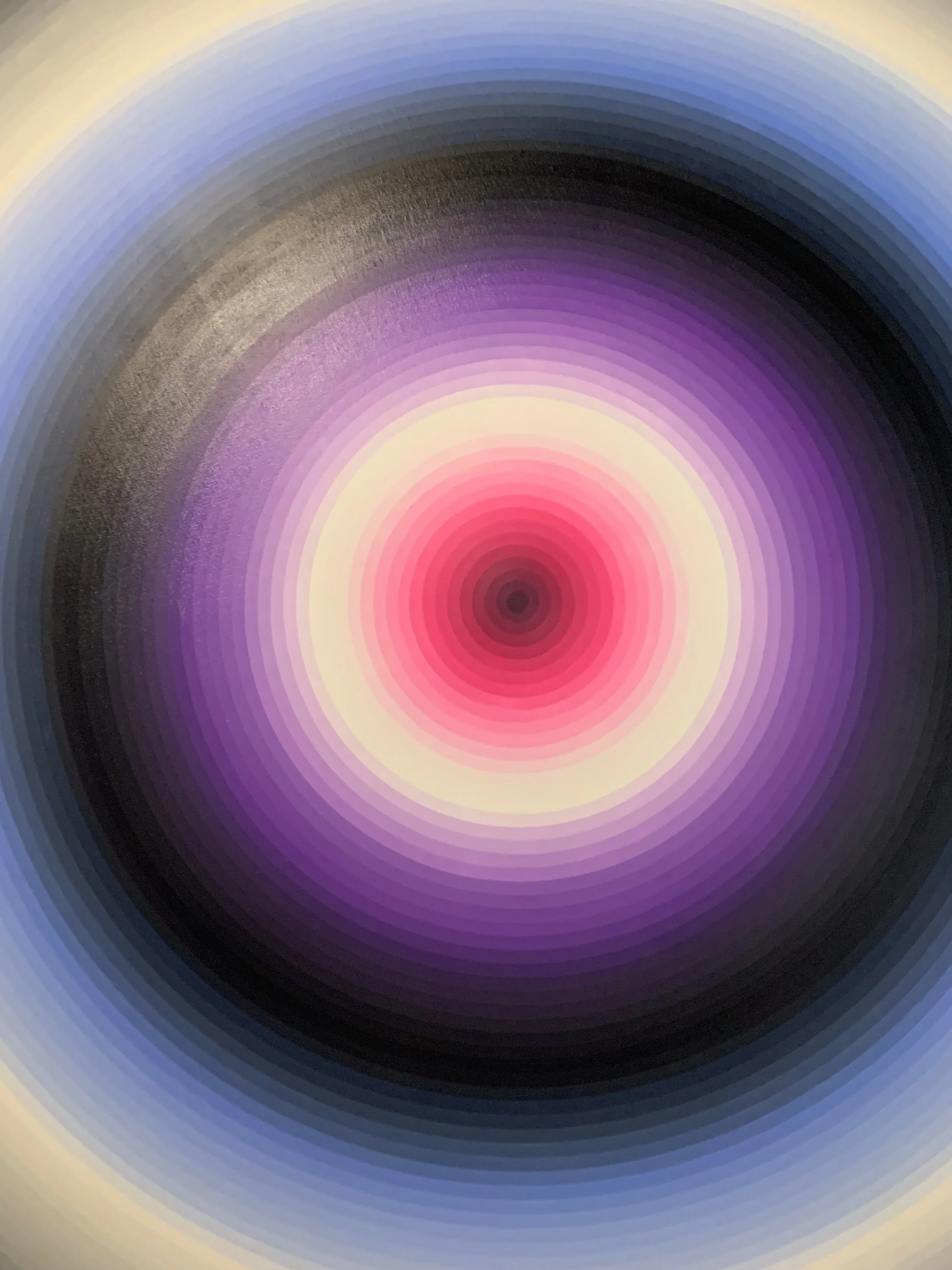 A close-up of a circular, colorful pattern with concentric rings in various shades of purple, pink, black, and purple.