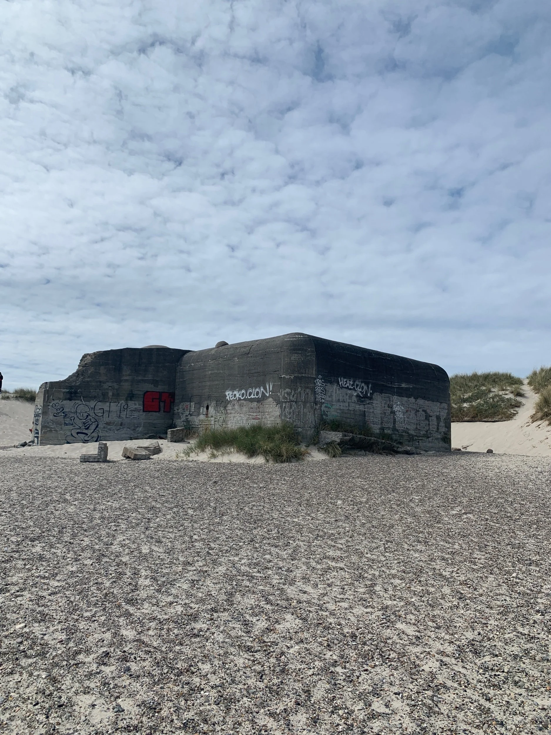 A concrete bunker with graffiti on it, situated on a sandy beach under a cloudy sky.