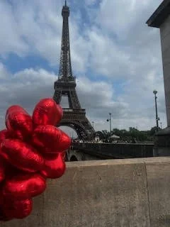 Red heart-shaped balloons held in front of the Eiffel Tower in Paris, France.