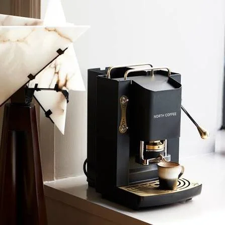 Black North Coffee espresso machine with a cup underneath, on a white countertop in a modern kitchen.