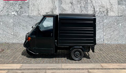 Small black cargo vehicle parked on sidewalk in front of a stone wall