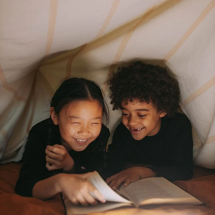 Two kids enjoying reading a book in a blanket fort