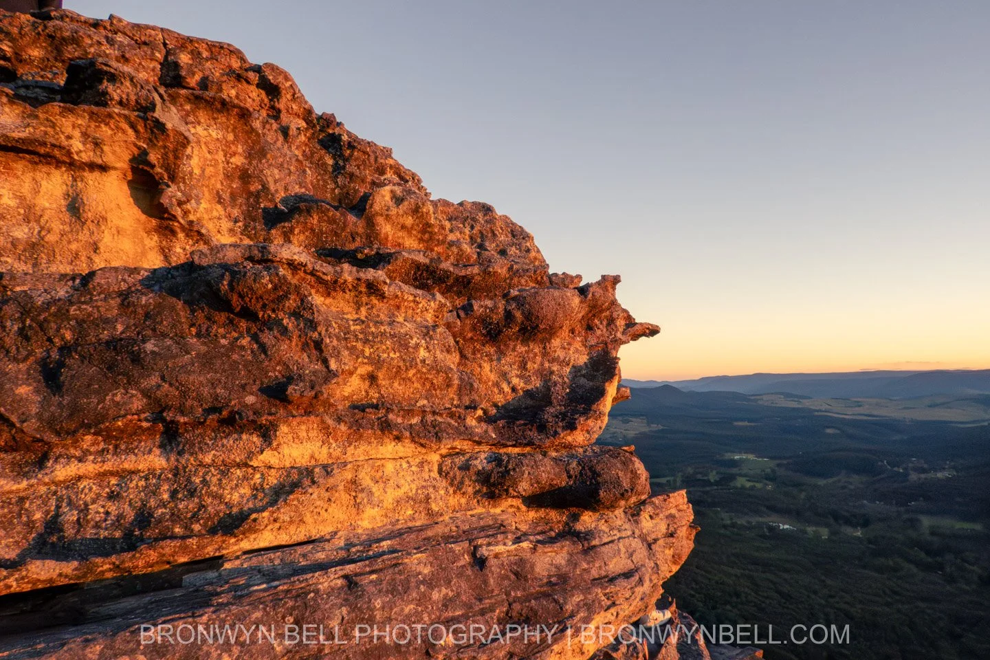 Close-up of the rocky outcrop at Sunset Rock in the Blue Mountains, showing sharp, grainy textures and rugged edges. The rock face is illuminated by warm orange and golden sunset light, highlighting its detailed surface.
