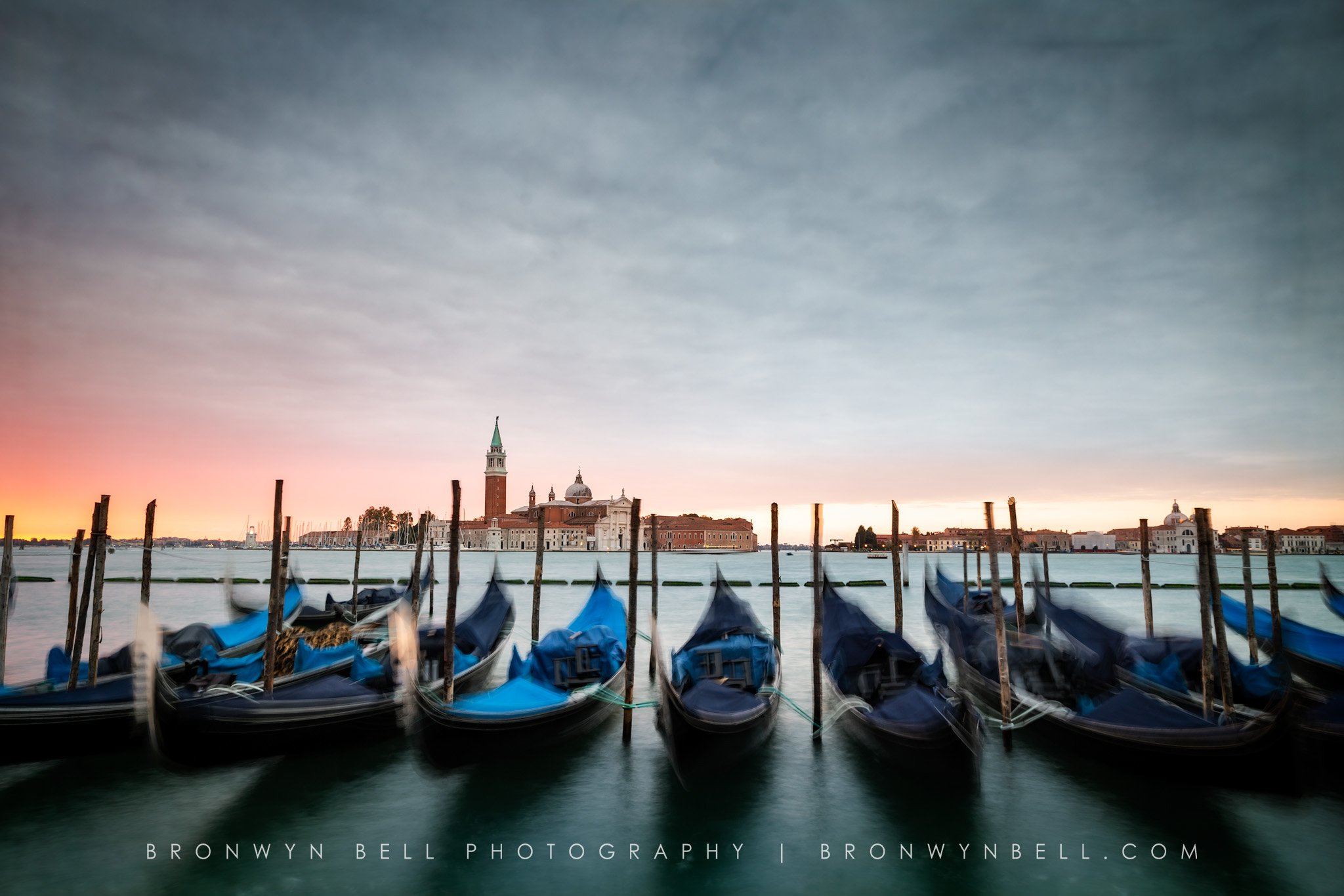 Gondolas docked on the water with buildings and a church in the background during sunset in Venice, Italy.