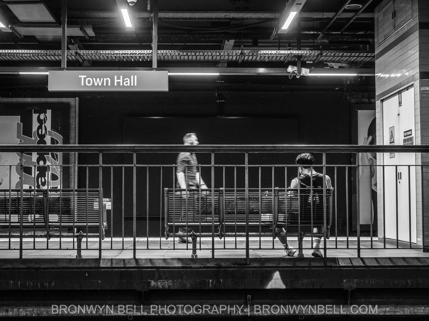 Black and white photograph of commuters waiting on the underground platform at Town Hall train station in Sydney while trains move through the station.