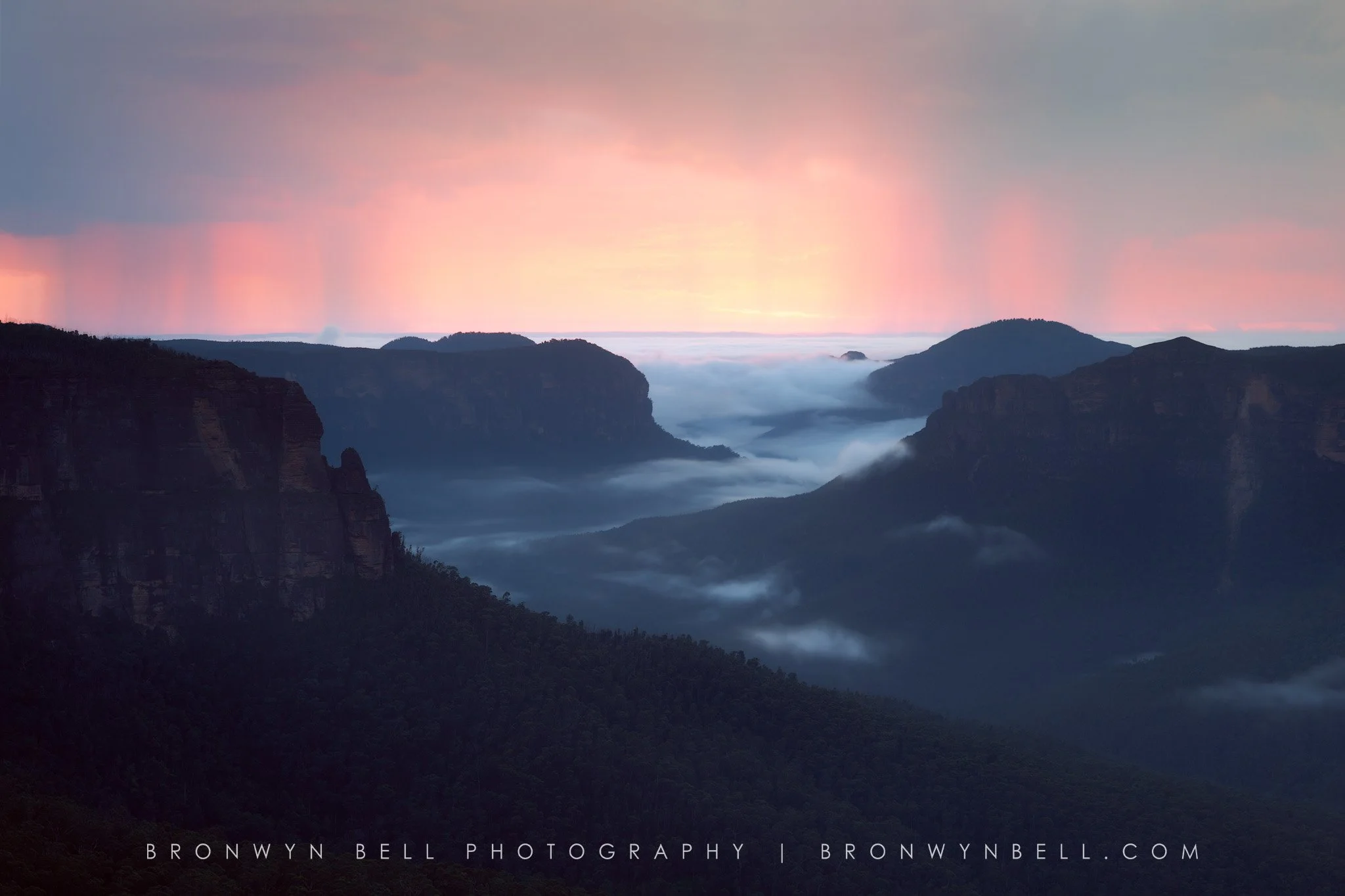 Sunrise over a mountain landscape with fog-filled valleys and pink and blue sky