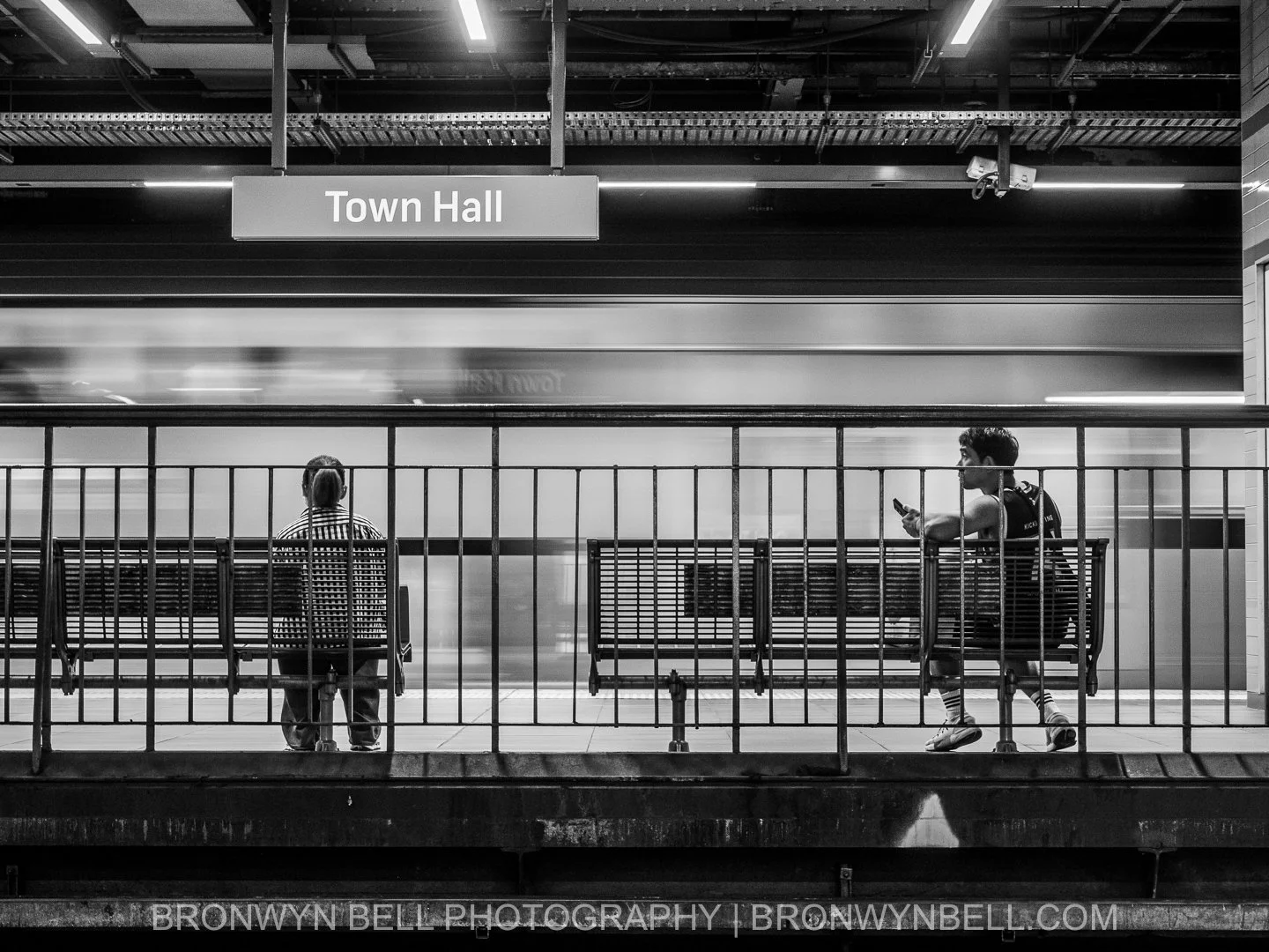 Black and white photograph of commuters waiting on the underground platform at Town Hall train station in Sydney while trains move through the station.