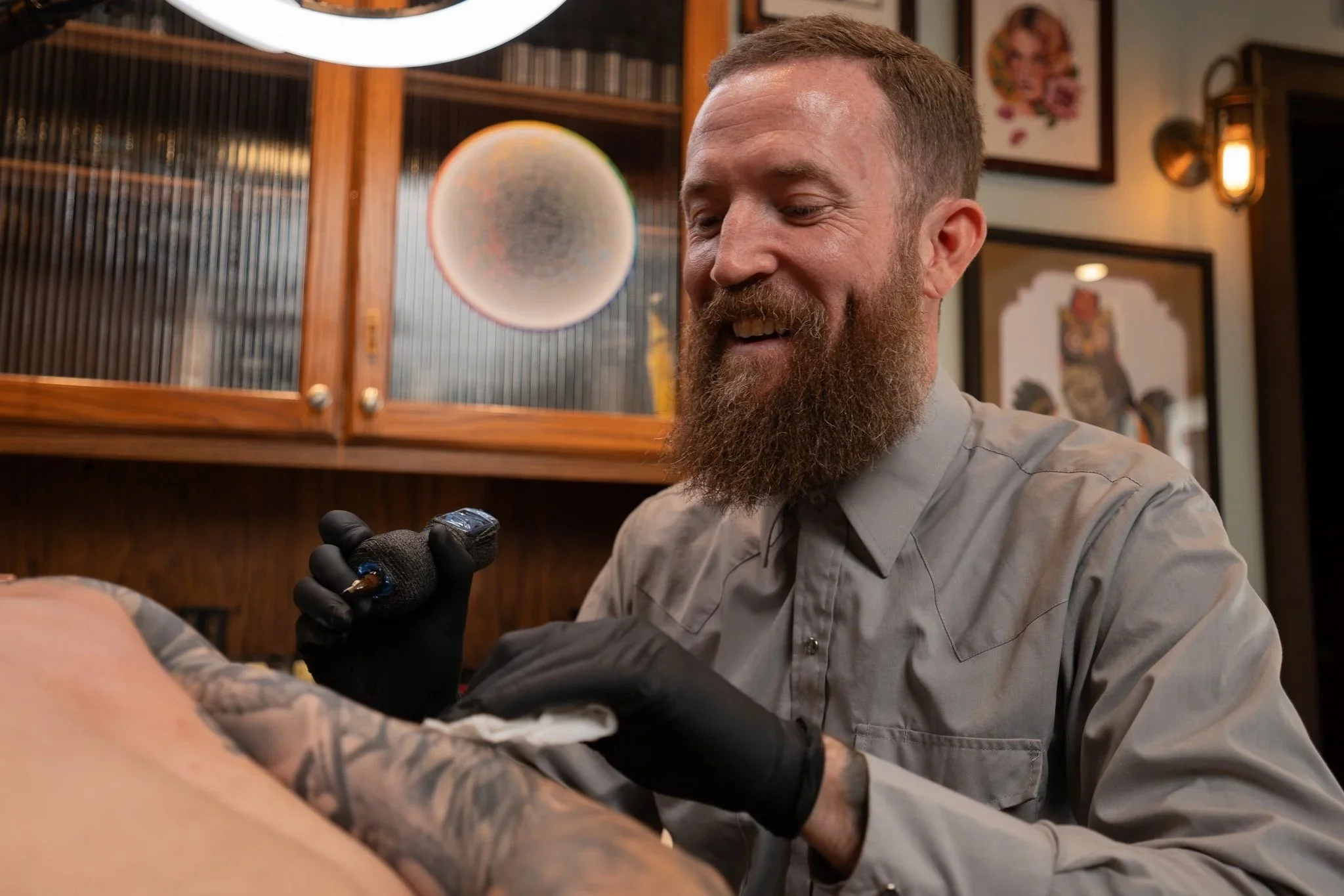 Tattoo artist wearing black gloves, creating a tattoo on a client's arm in a tattoo parlor.