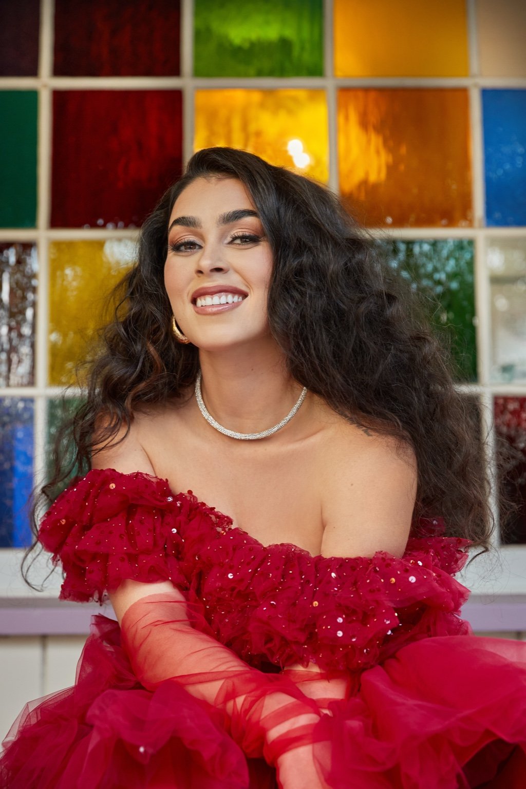 Natacha Karam, founder of Creativity Crew, smiling in a red tulle dress in front of a colourful stained-glass window