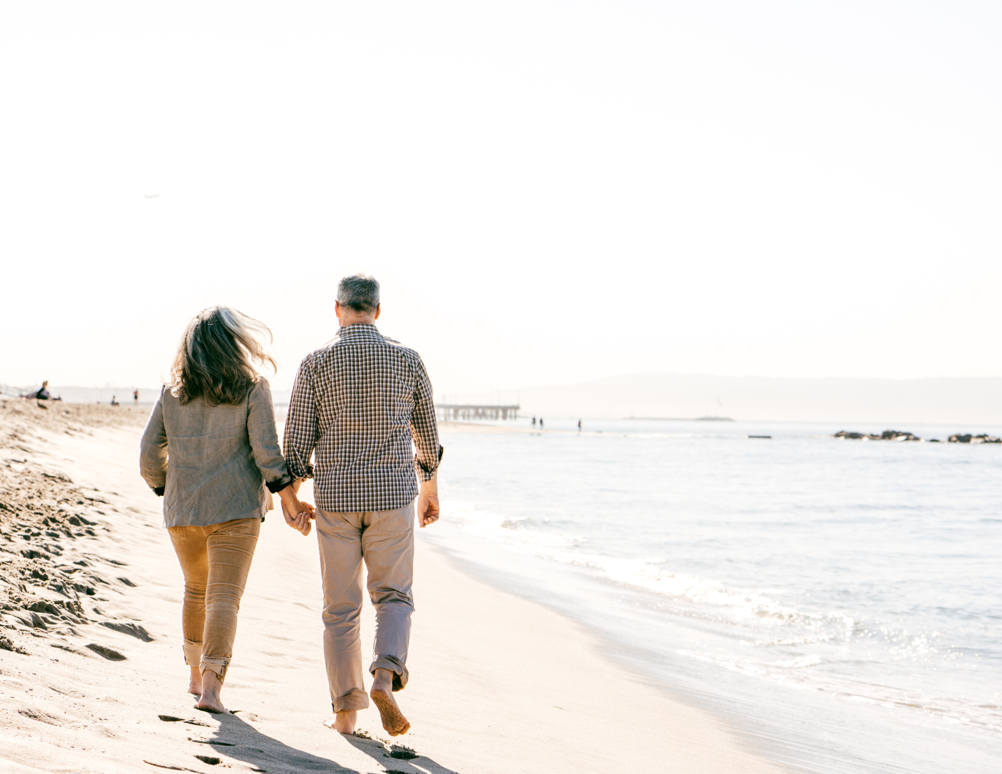 A couple holding hands walking along the beach near the shoreline with the ocean in the background.