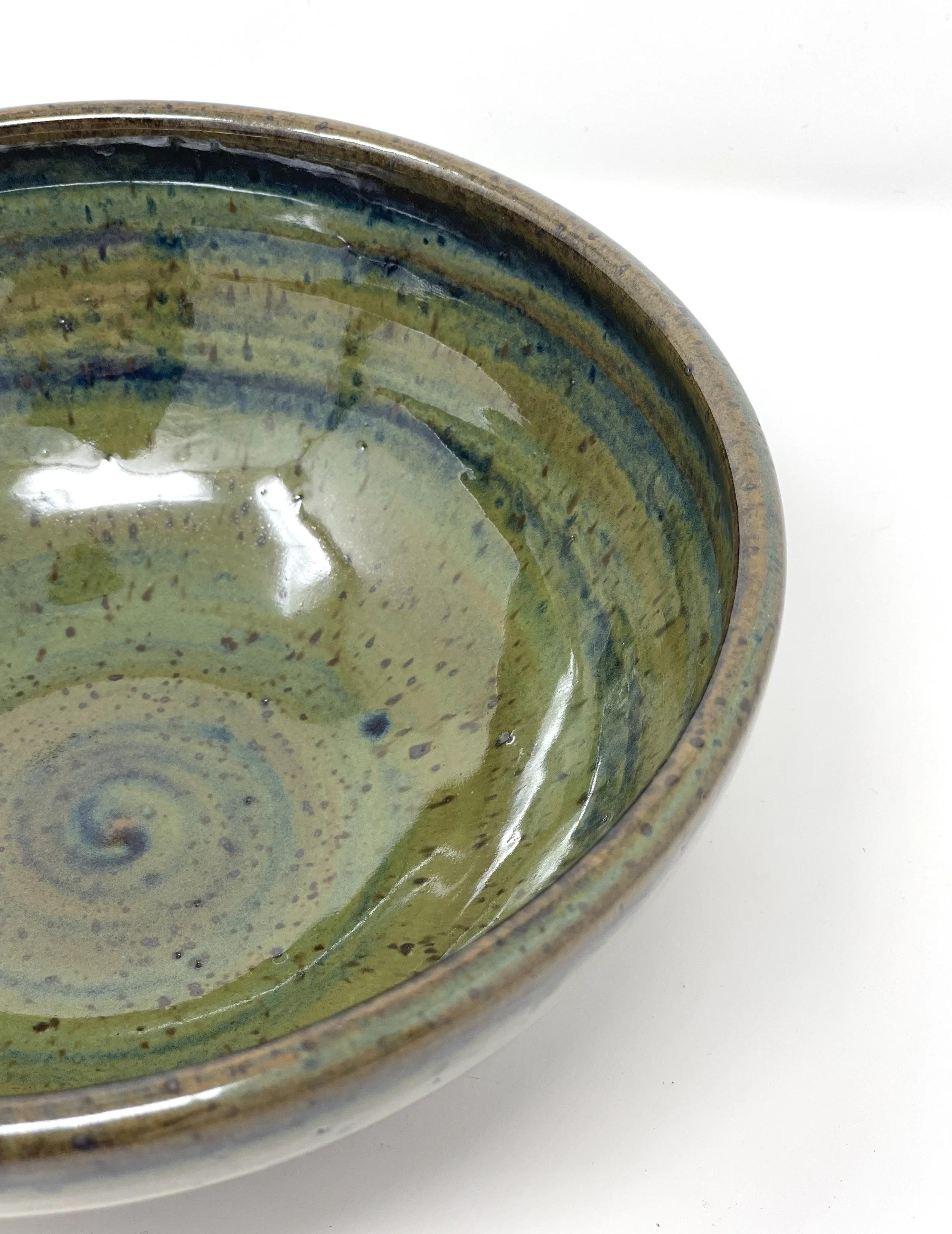 Close-up of a ceramic bowl with green and blue glaze, showing spiral and dotted patterns on the inside.