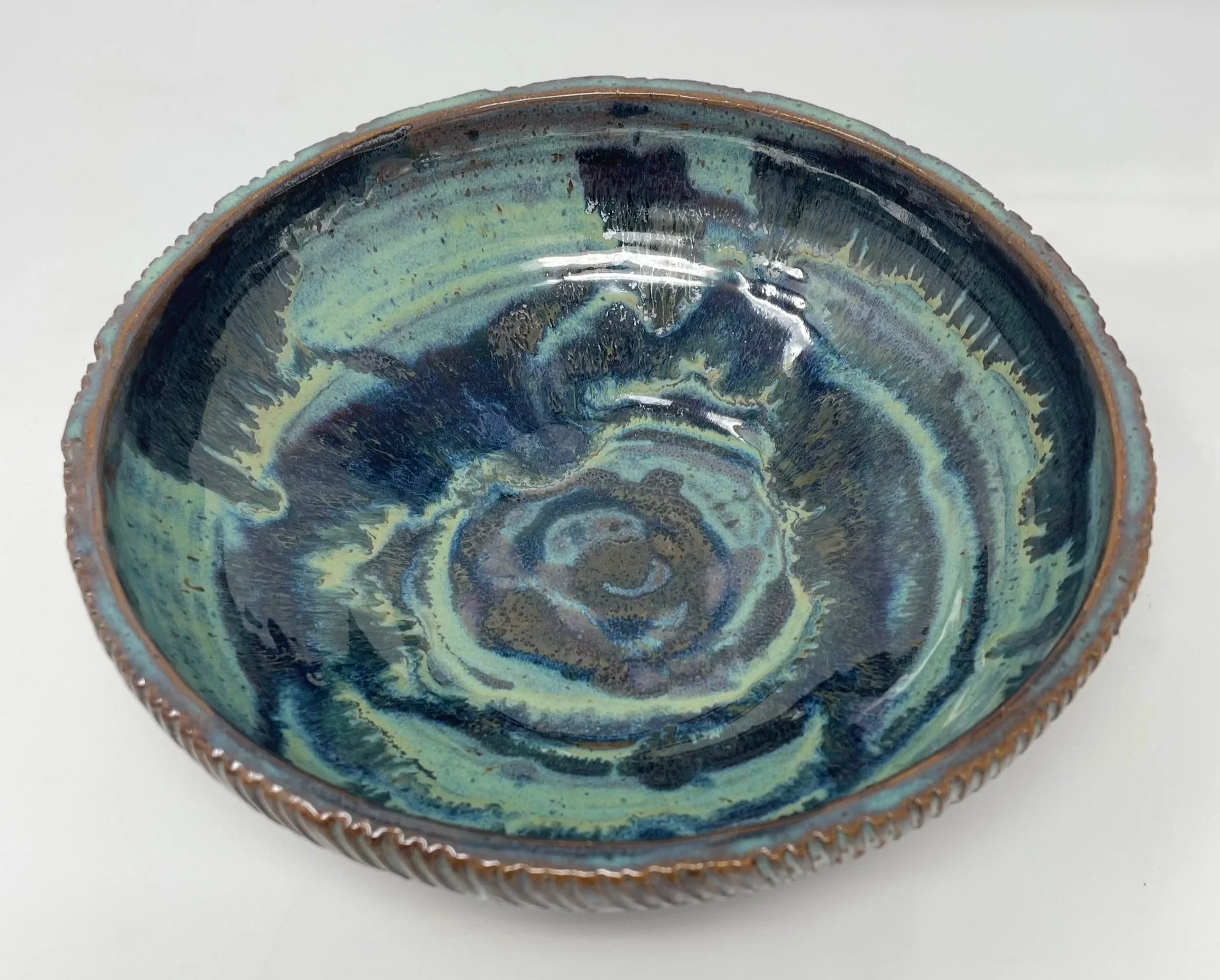 A ceramic bowl with a blue, green, and black glaze design, featuring a textured exterior rim.