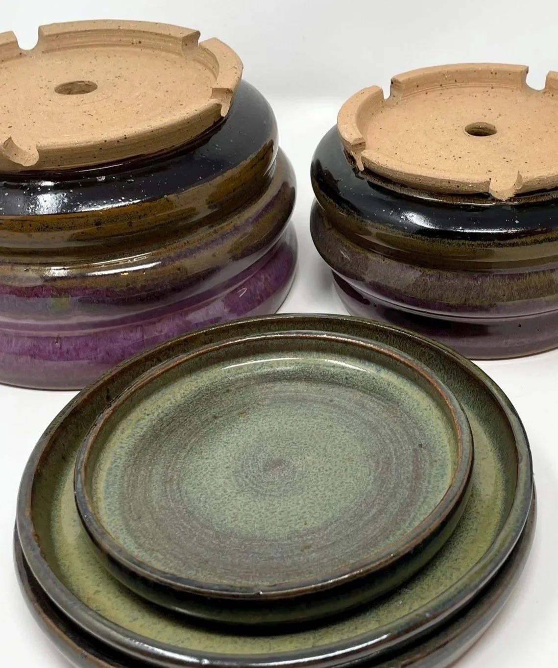 Stacked ceramic planters with plates with unglazed bottoms, set against a white background.