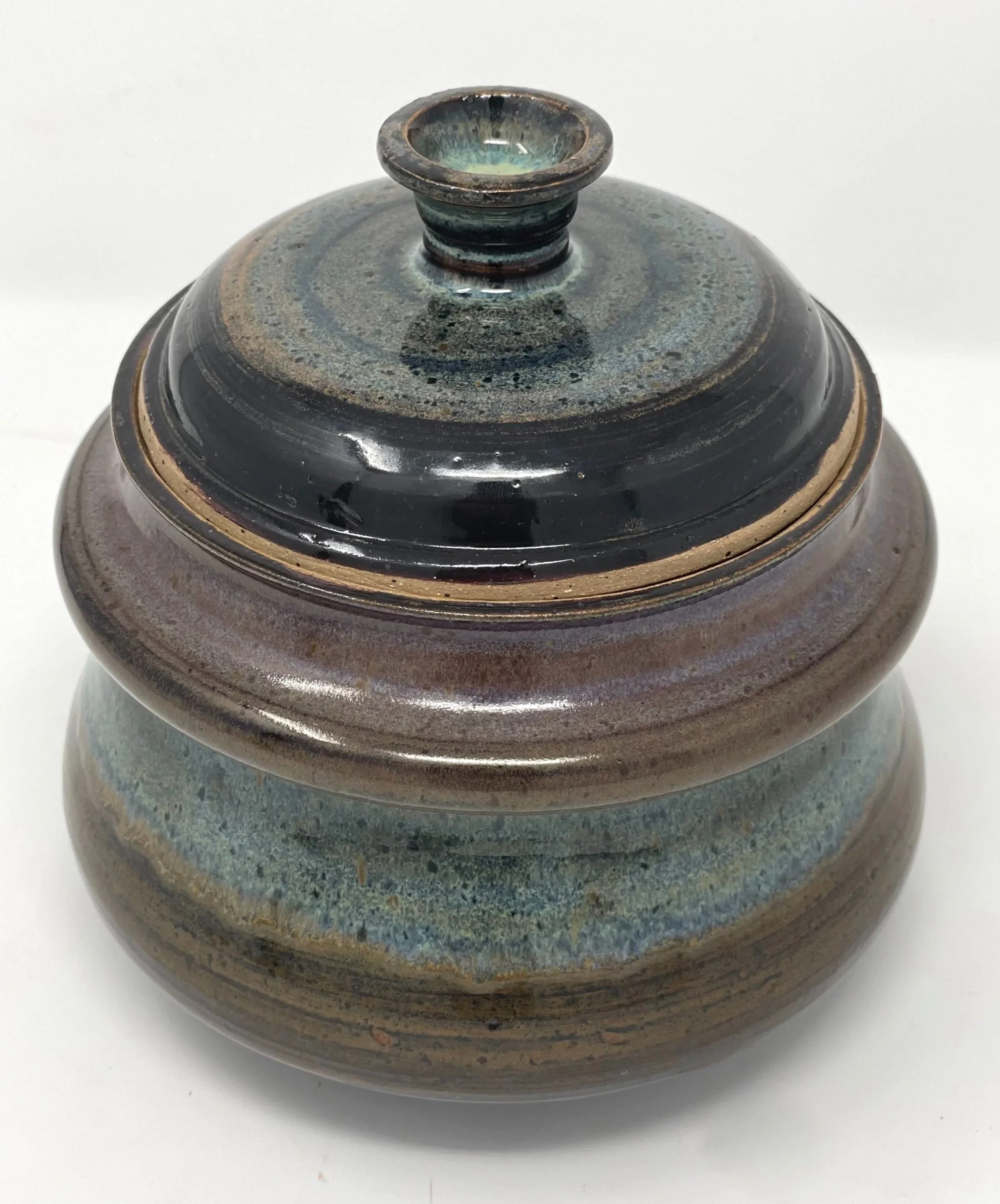 A glazed ceramic jar with a lid, featuring earthy tones and a textured blue and purple band around the middle.