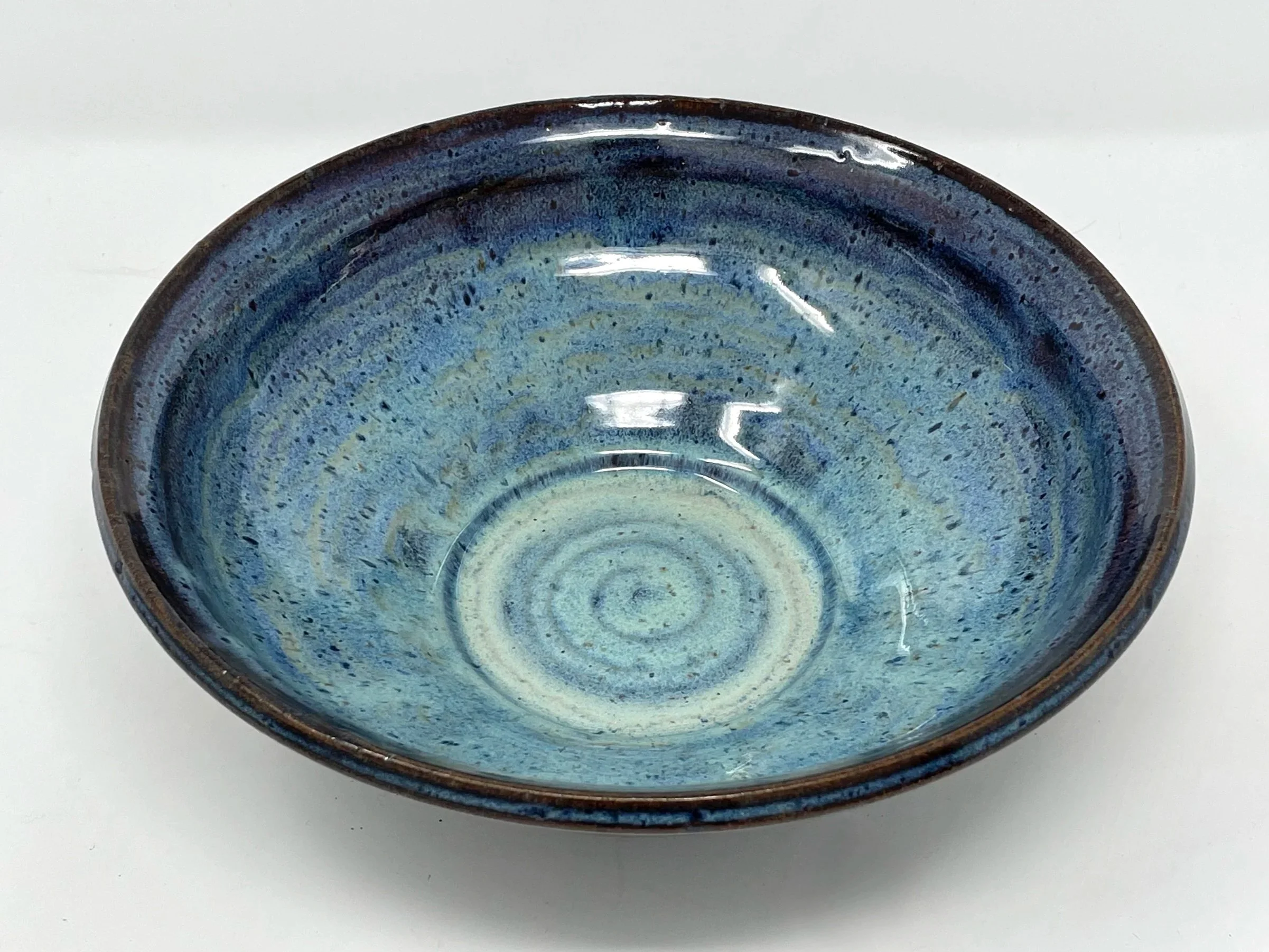 A ceramic bowl with a blue glaze and a spiral pattern at the bottom, placed on a white surface.