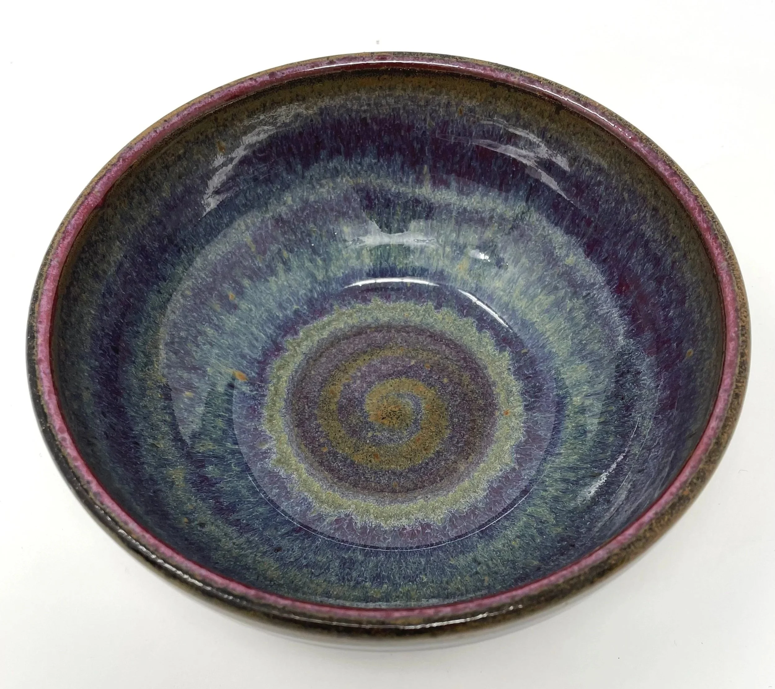 Close-up of a ceramic bowl with a spiral pattern and dark glaze on a white surface.