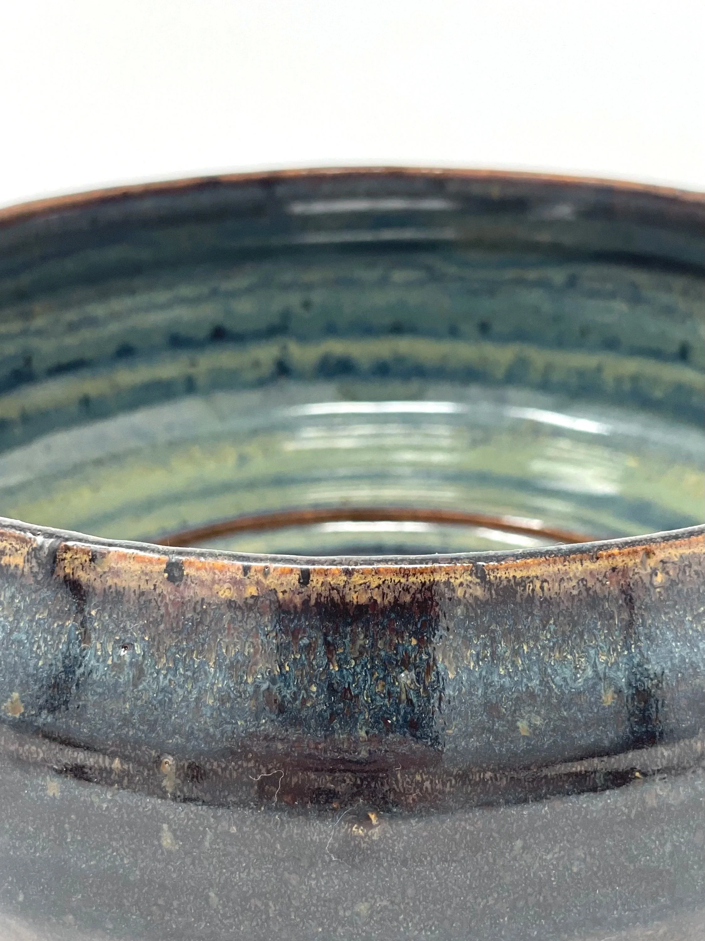 Close-up of the rim of a ceramic or pottery bowl with a rustic, textured finish in dark colors, showing slight rust and aging.