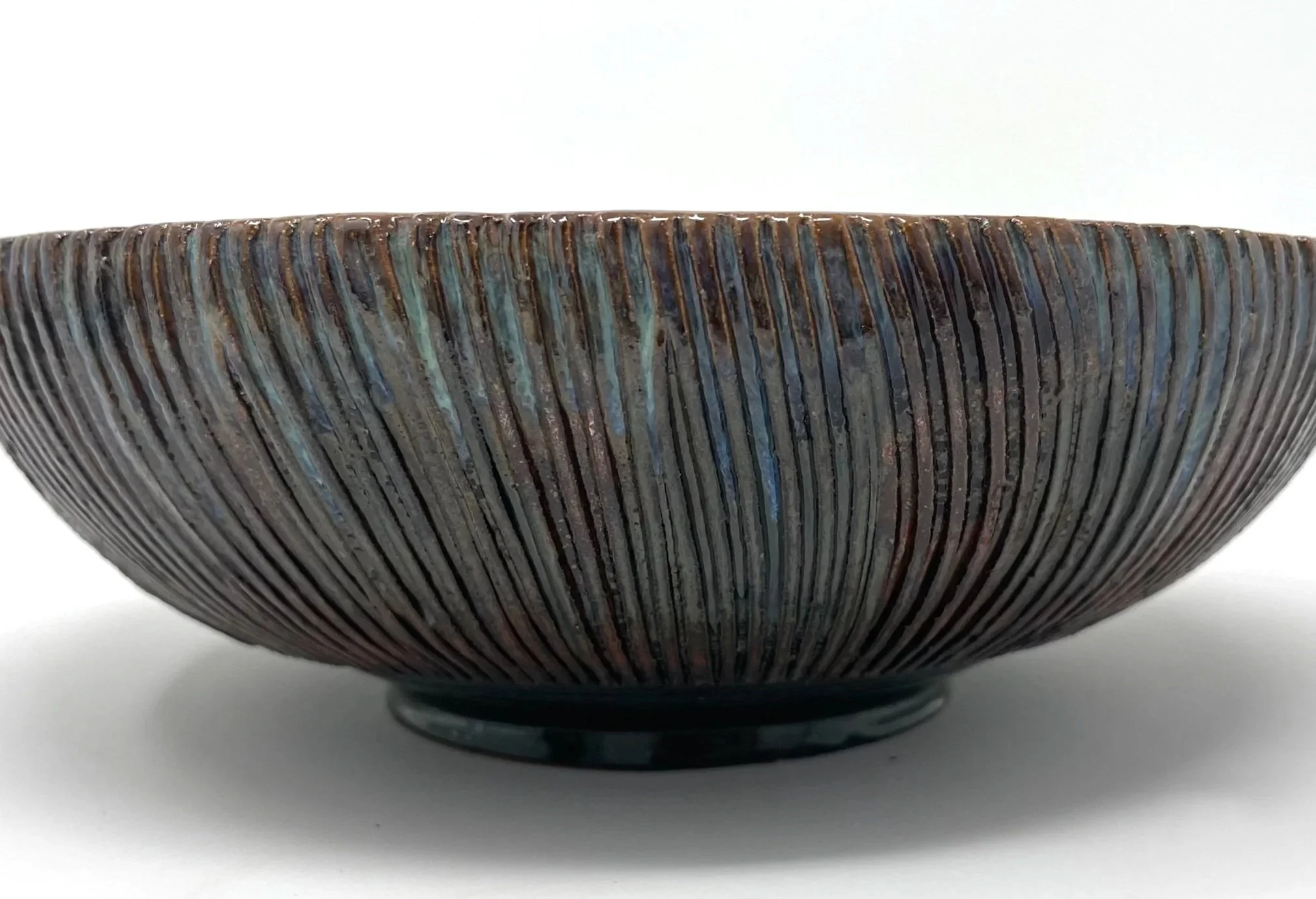 Close-up of a ceramic bowl with a textured, striped pattern and an iridescent glaze.