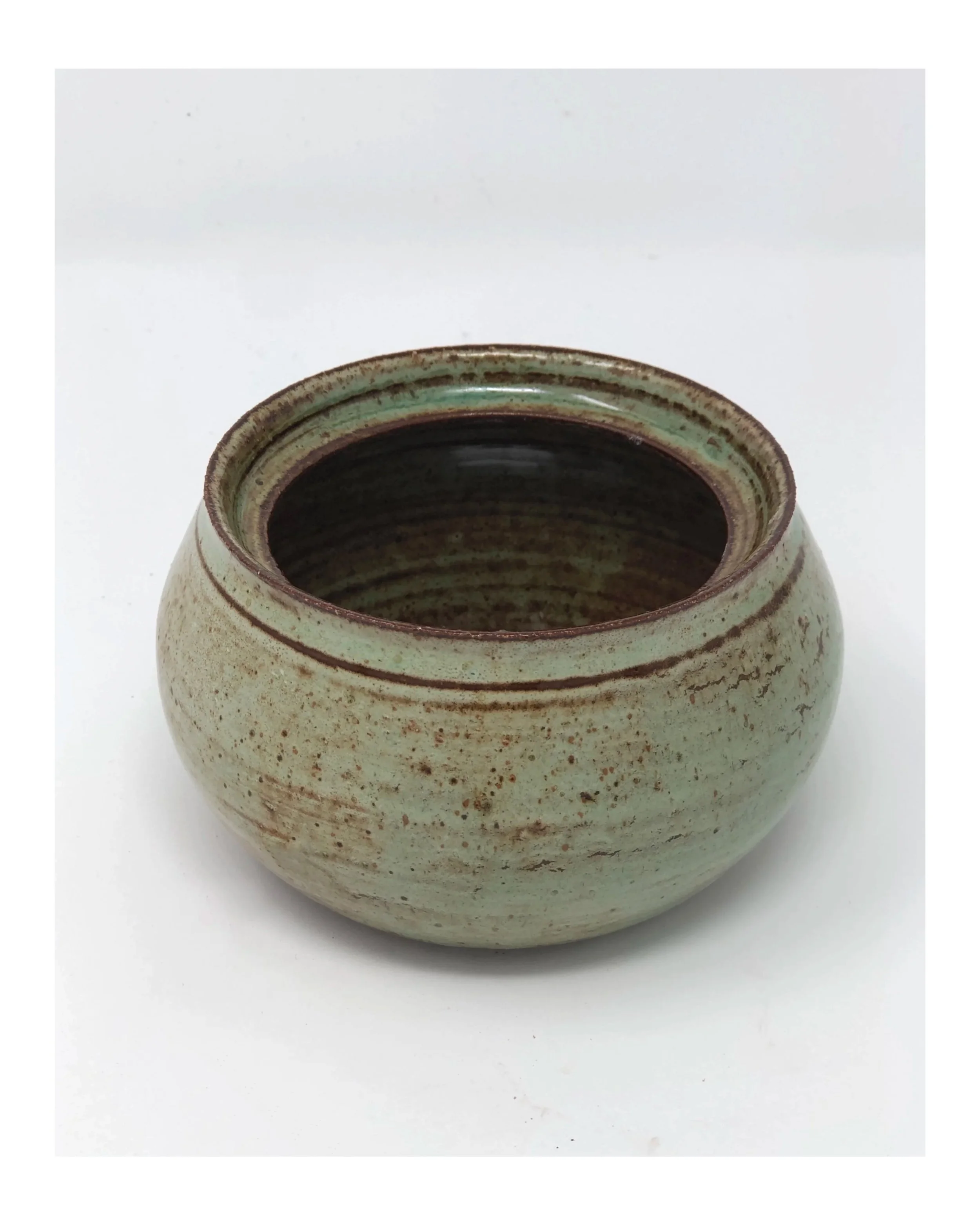 A round ceramic bowl with a greenish glaze and brown accents, sitting on a white surface.