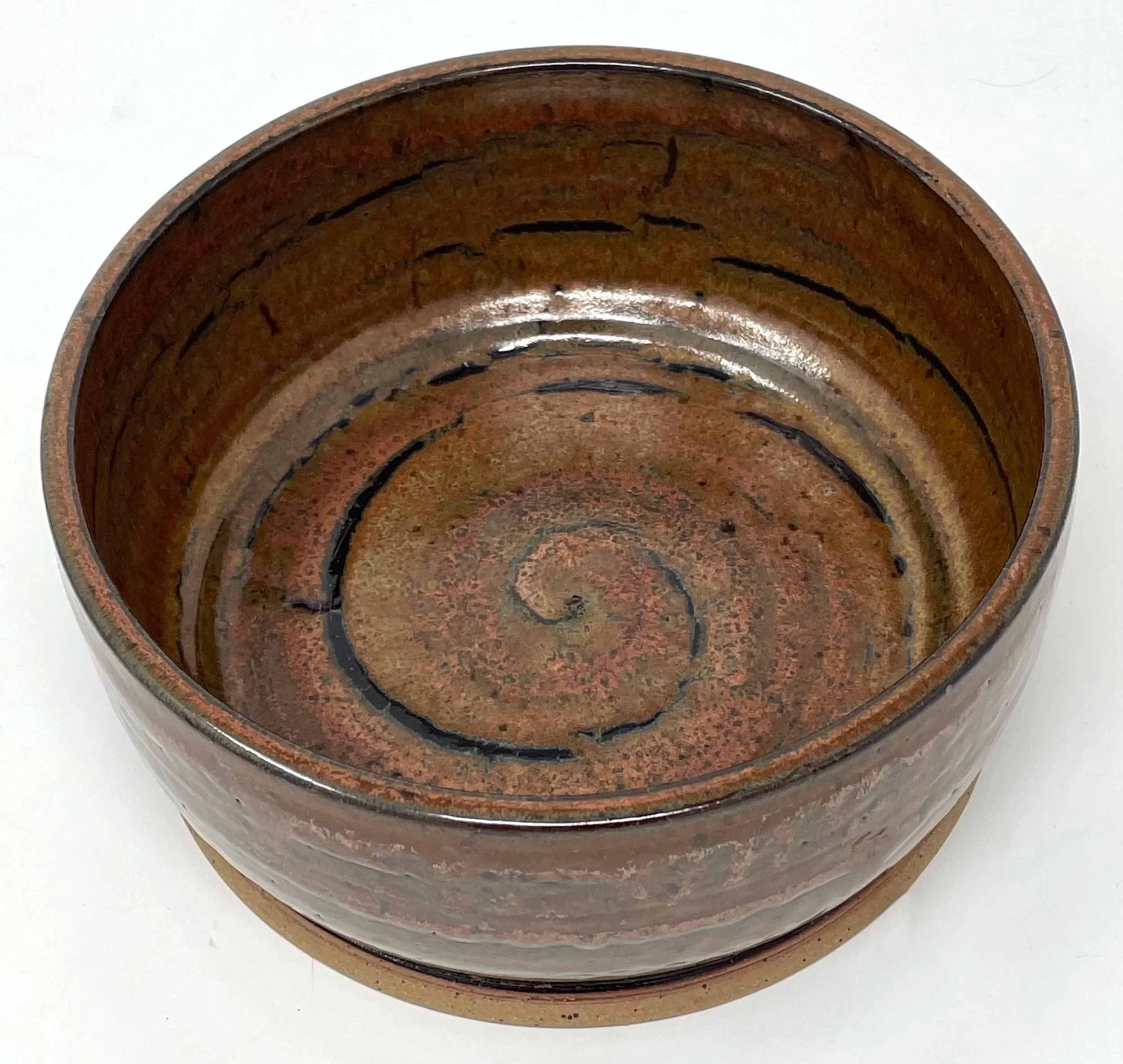 Round ceramic or clay pot with a spiral pattern and a glazed interior surface, placed on a white background.