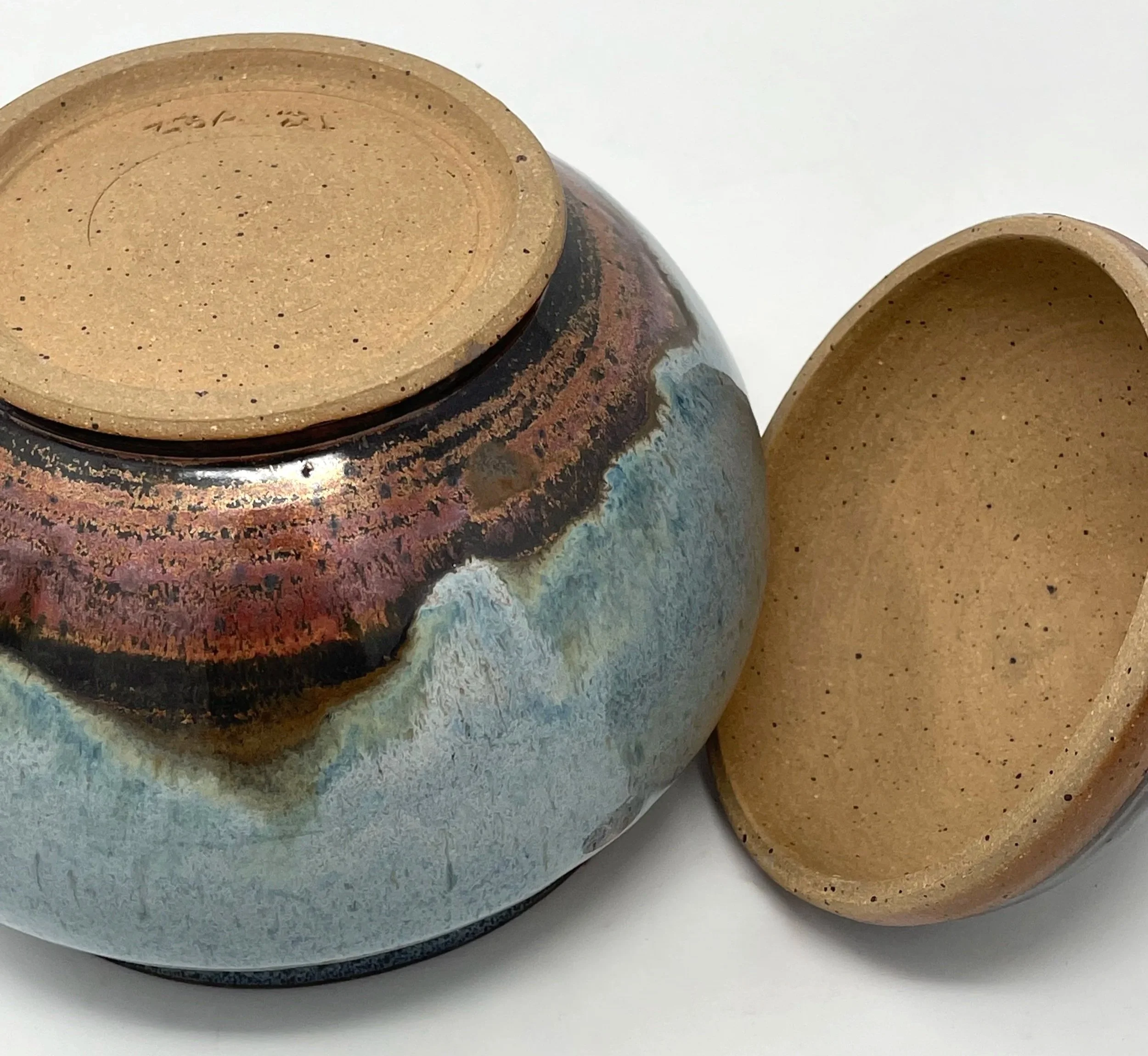 Two glazed ceramic bowls with earth-tone colors, one turned upside down showing the unglazed bottom, and the other with an open top, placed on a white surface.