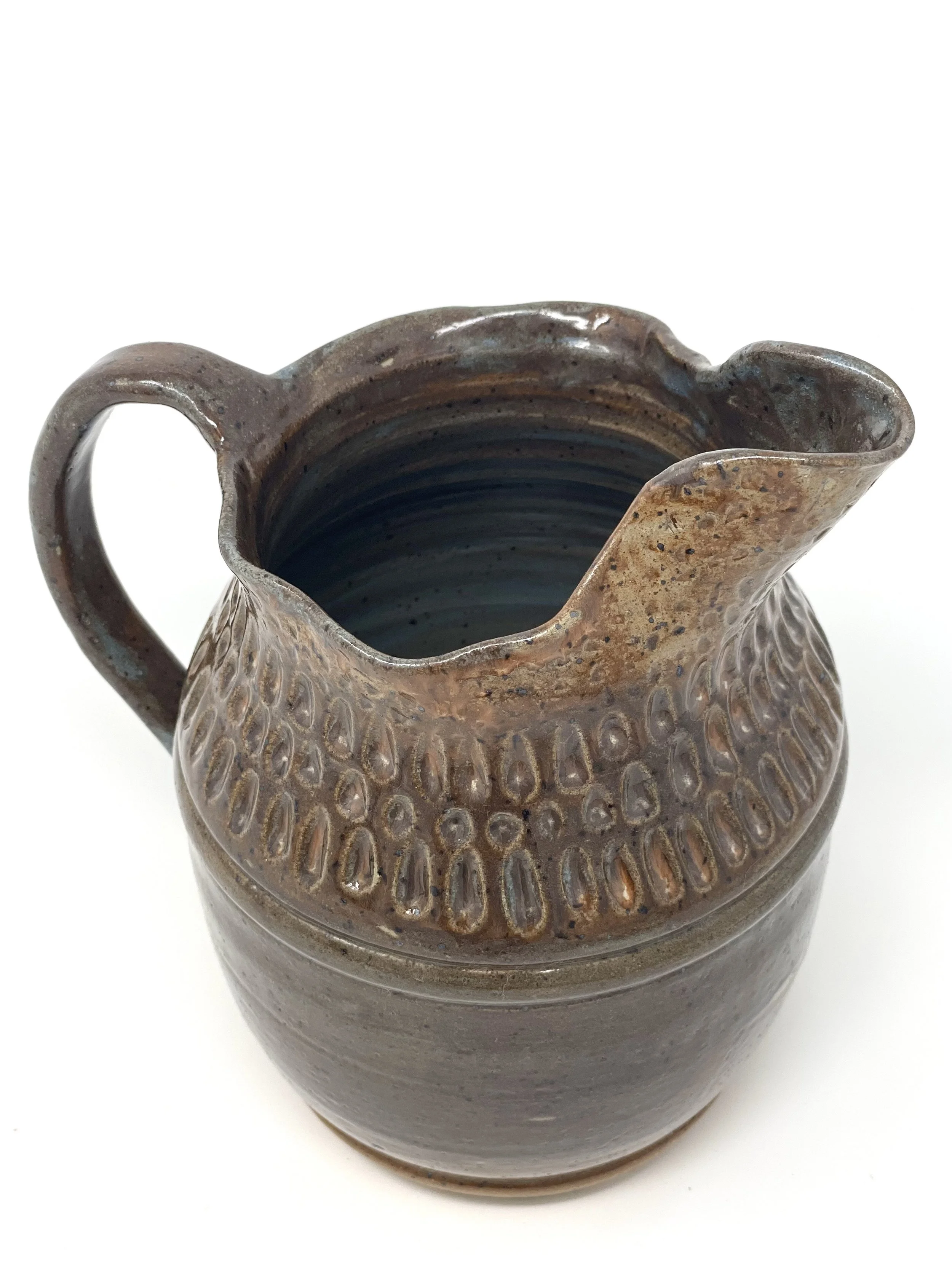 Brown ceramic pitcher with textured pattern and a spout, viewed from above on a white background.