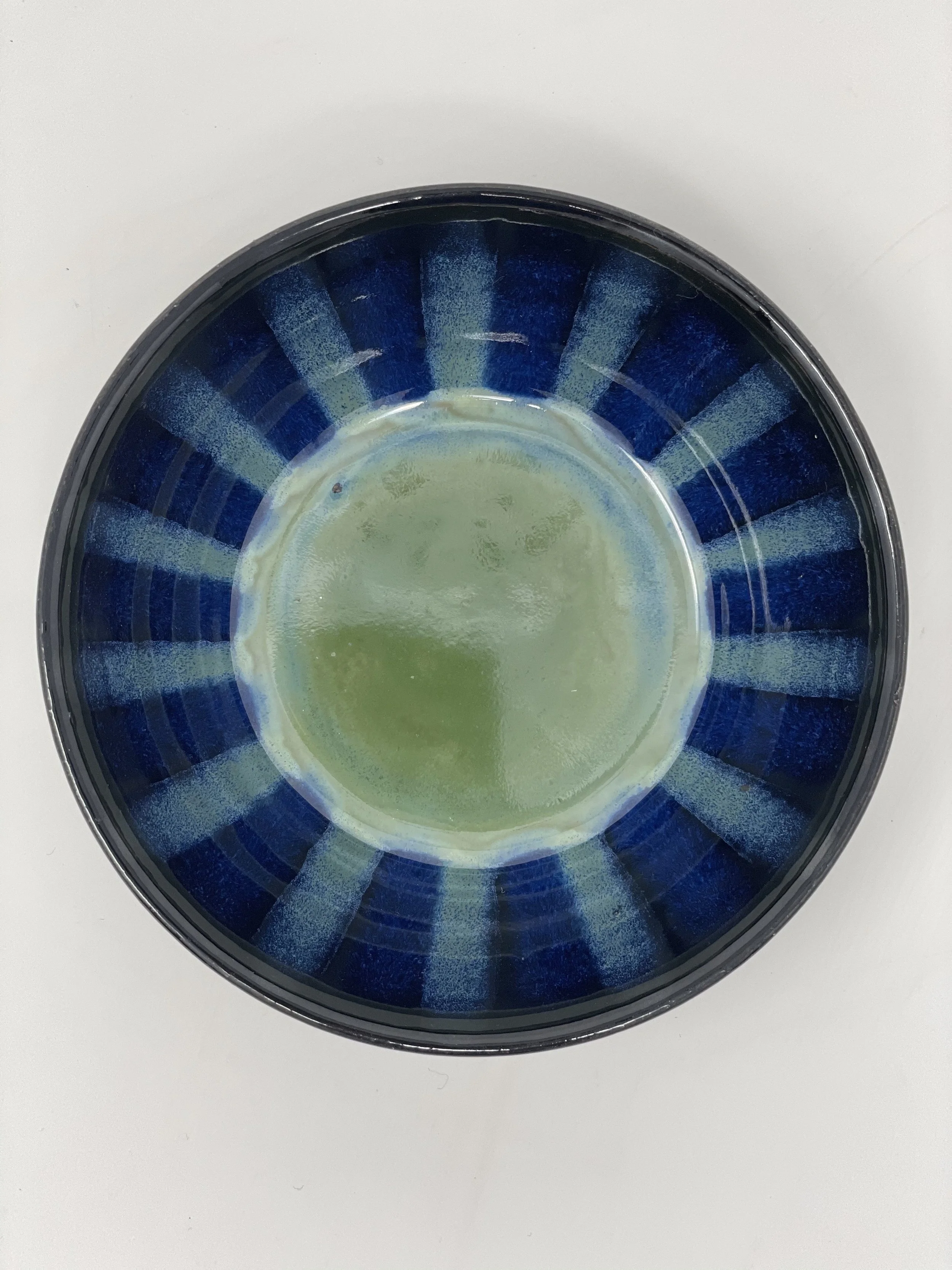 A round ceramic bowl with a blue exterior and a green and blue interior, sitting on a white surface.