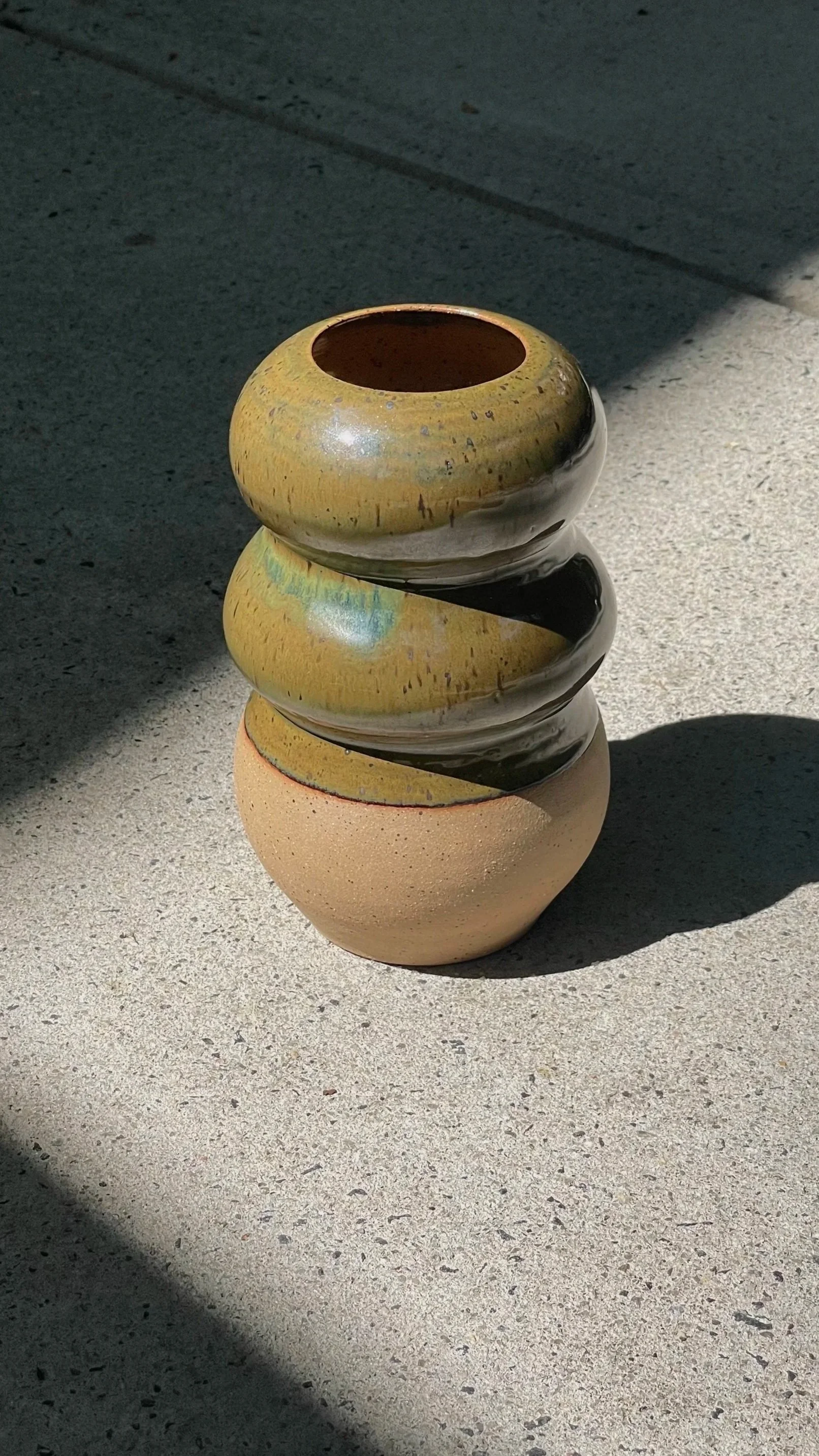 A tall bubble green pottery vase on concrete ground with shadows.
