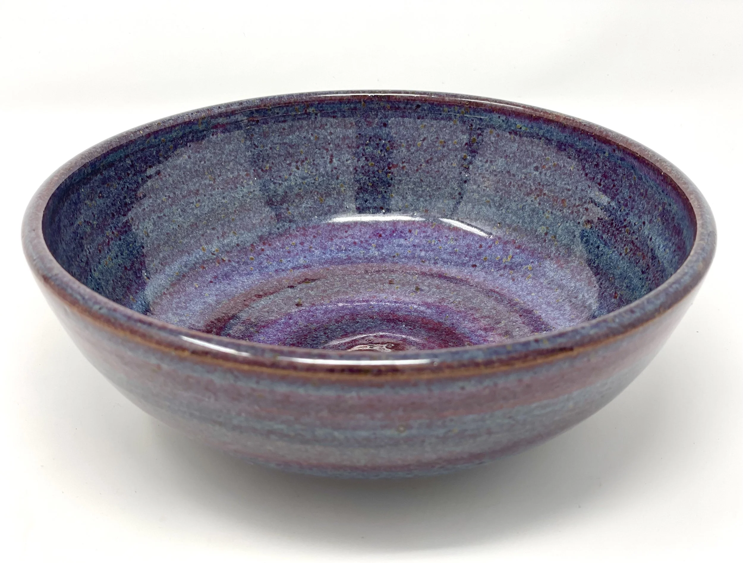 A ceramic bowl with a multicolored glaze in shades of purple, blue, and pink, on a white background.