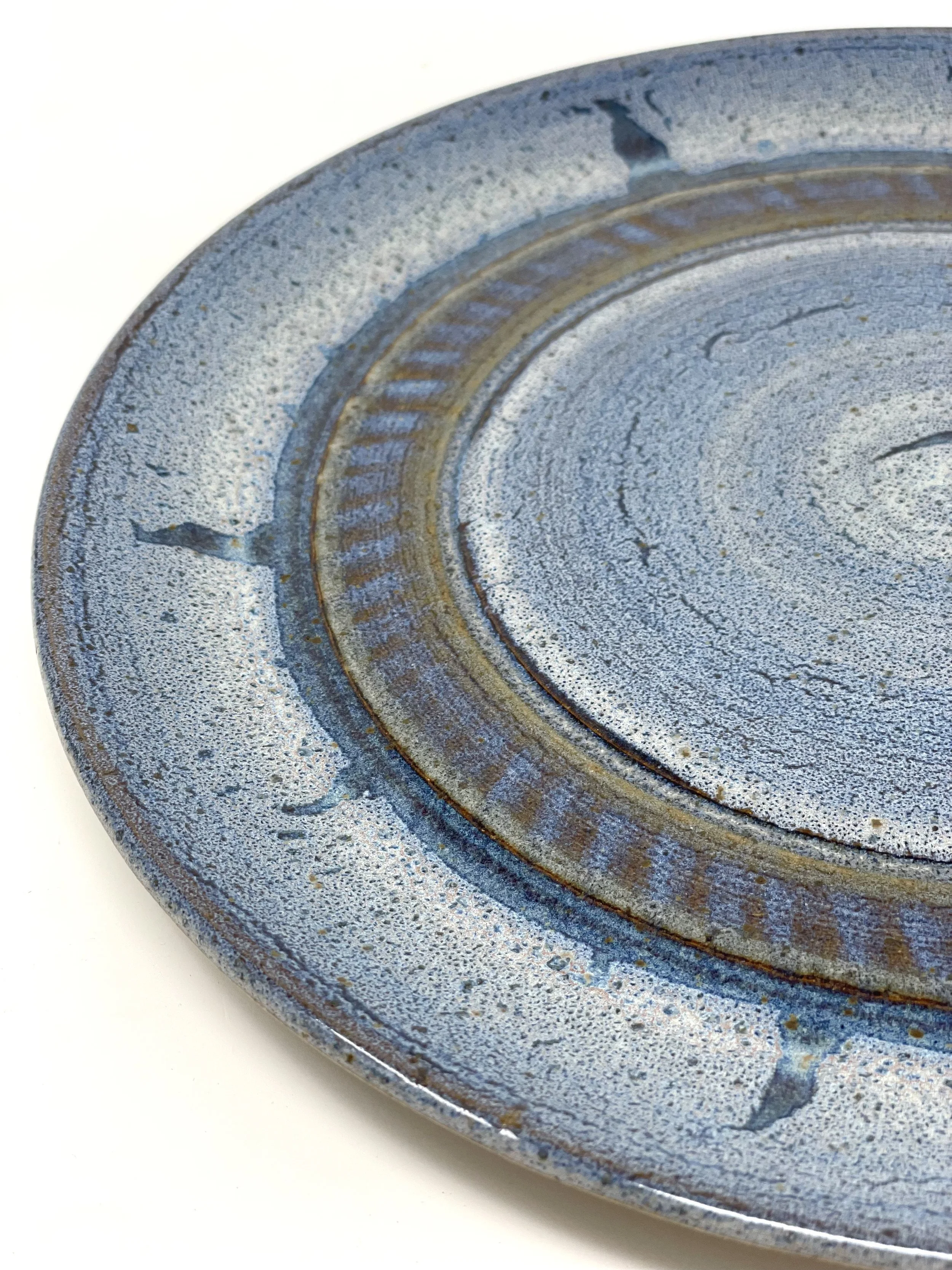 Close-up of a circular, metallic, blue-grey ceramic plate with textured surface and rust-colored accents.