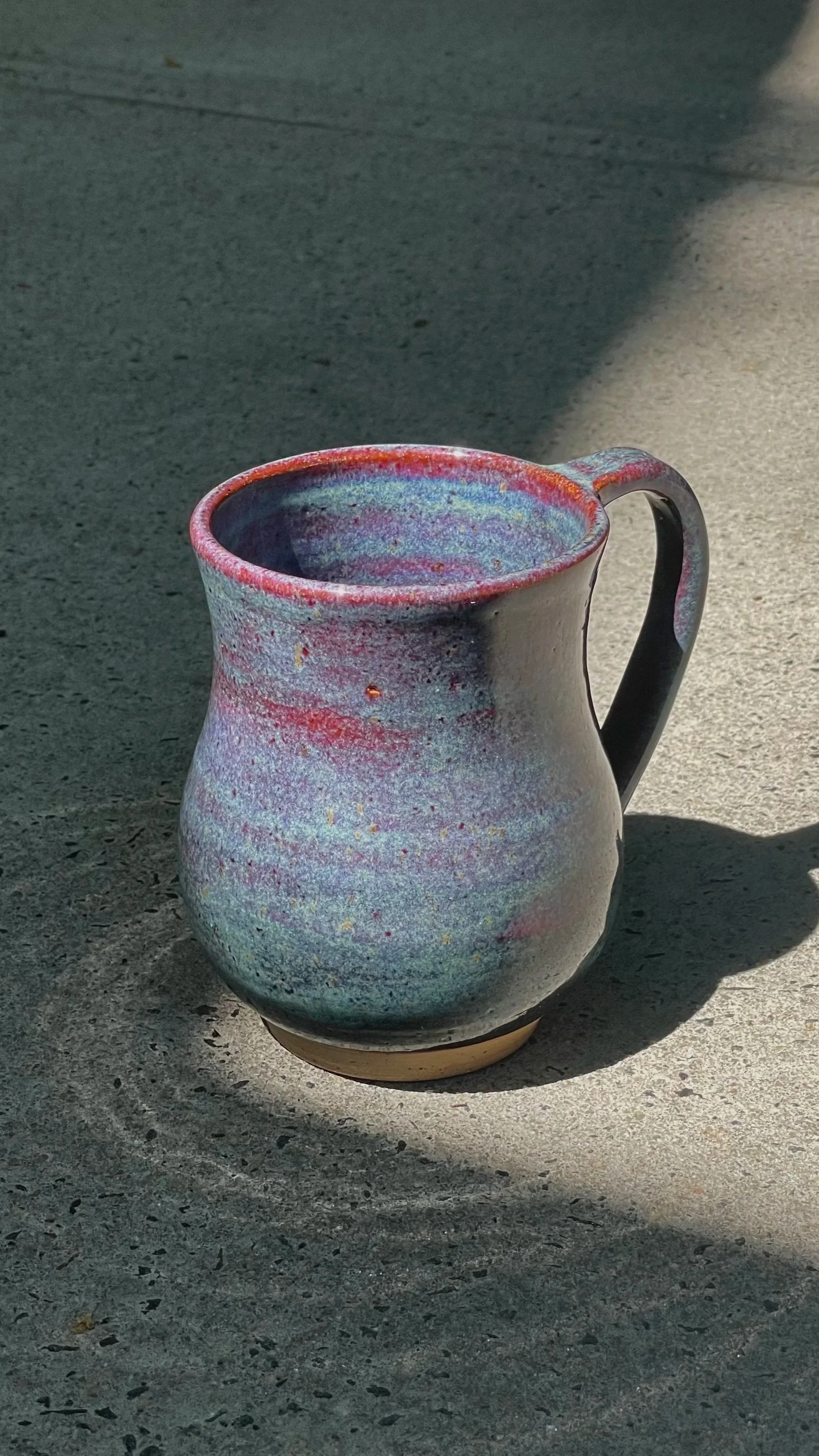 A ceramic mug with a colorful cotton candy glaze sits on a concrete surface, casting a shadow to the right.