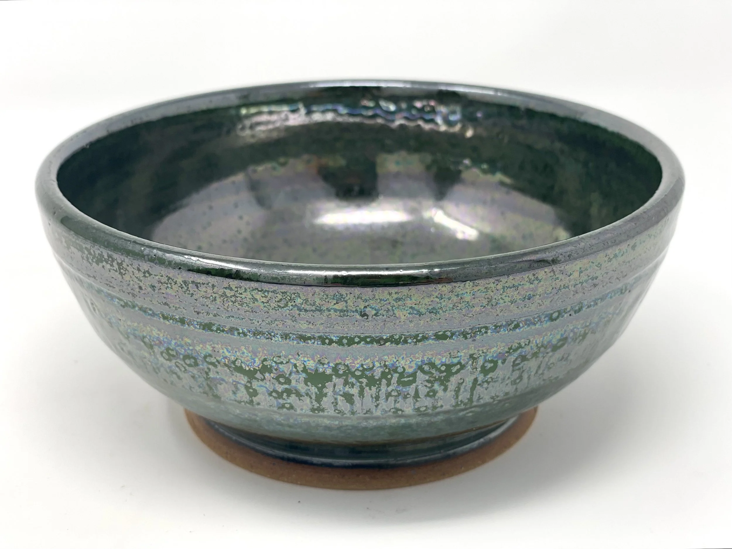 A ceramic bowl with a glazed greenish finish and a textured exterior, placed on a small round wooden coaster.