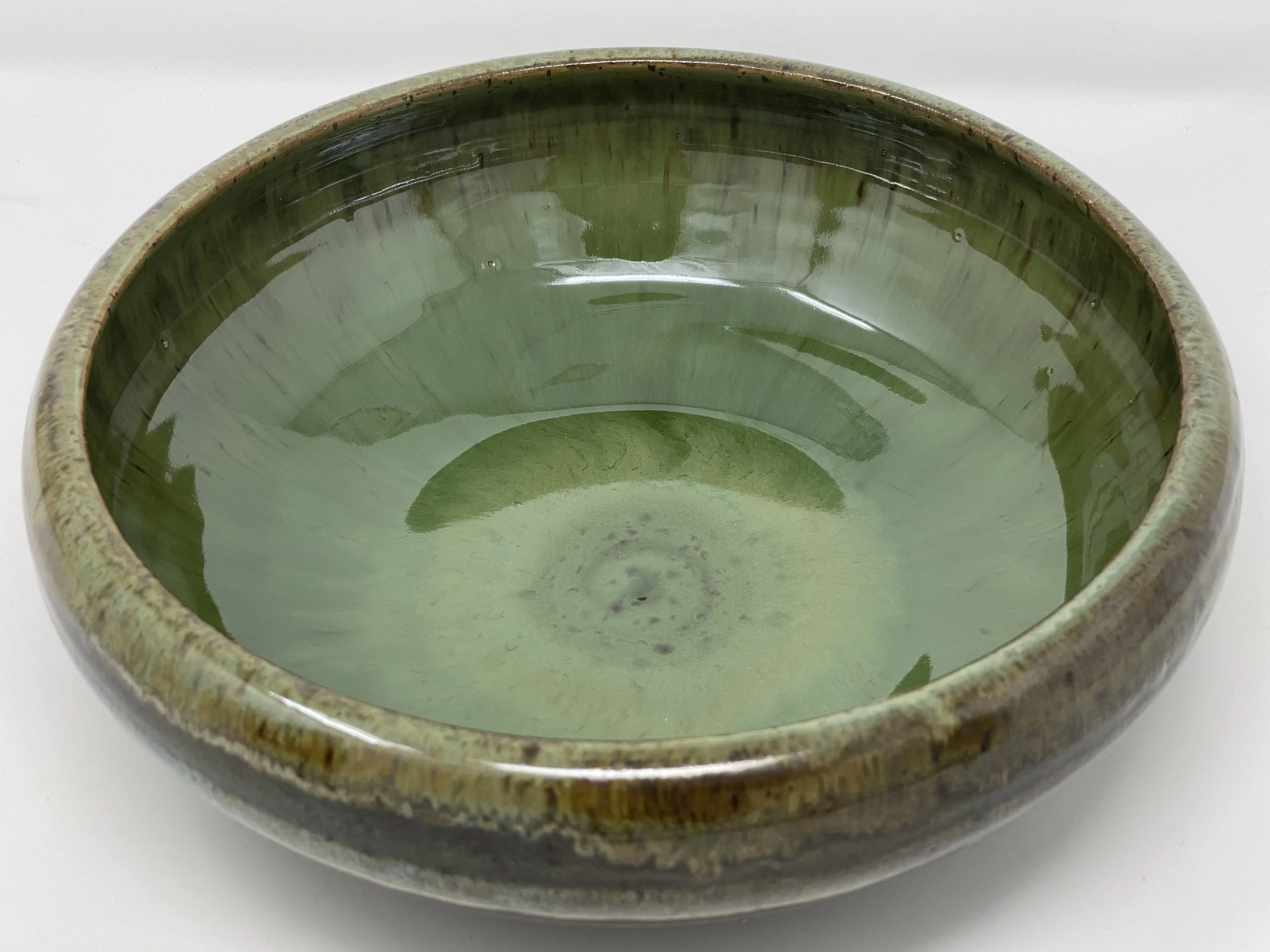 A glossy ceramic bowl with a green glaze, filled with water, placed on a white surface.