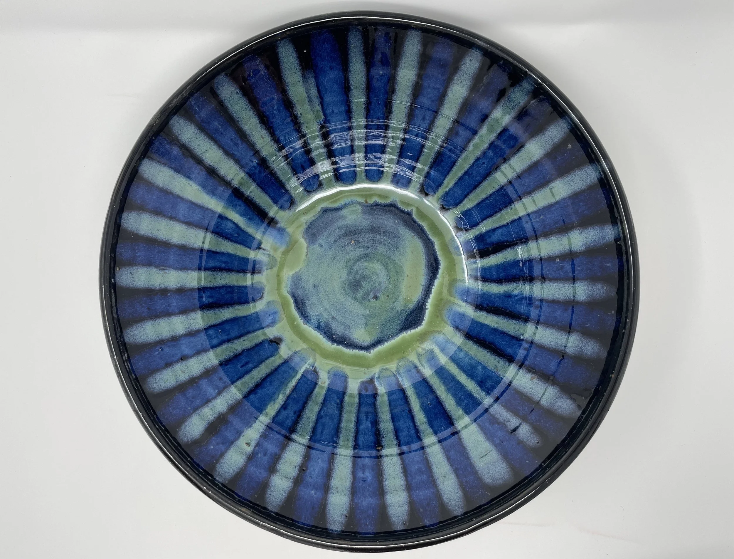 A round ceramic bowl with a blue, green, and black sun glaze pattern, viewed from above on a plain white surface.