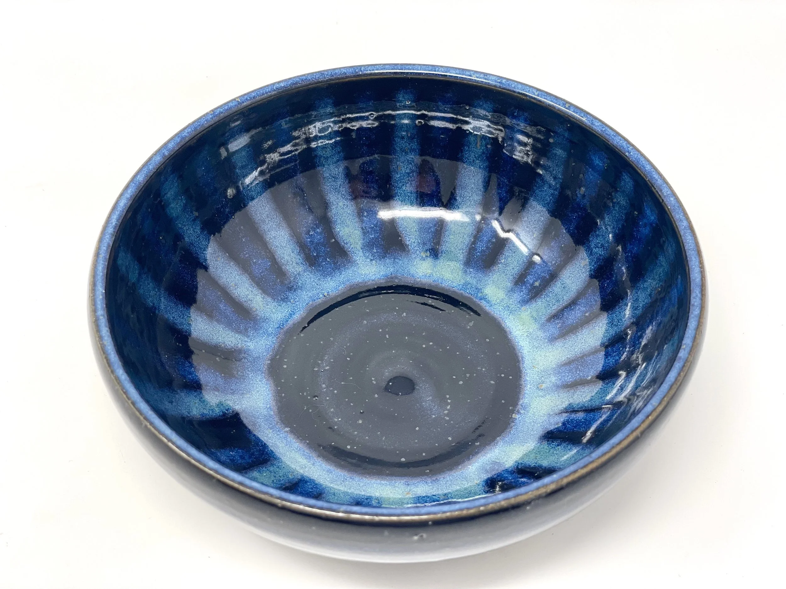 Blue ceramic bowl with a ribbed pattern and speckled interior, placed on a white surface.