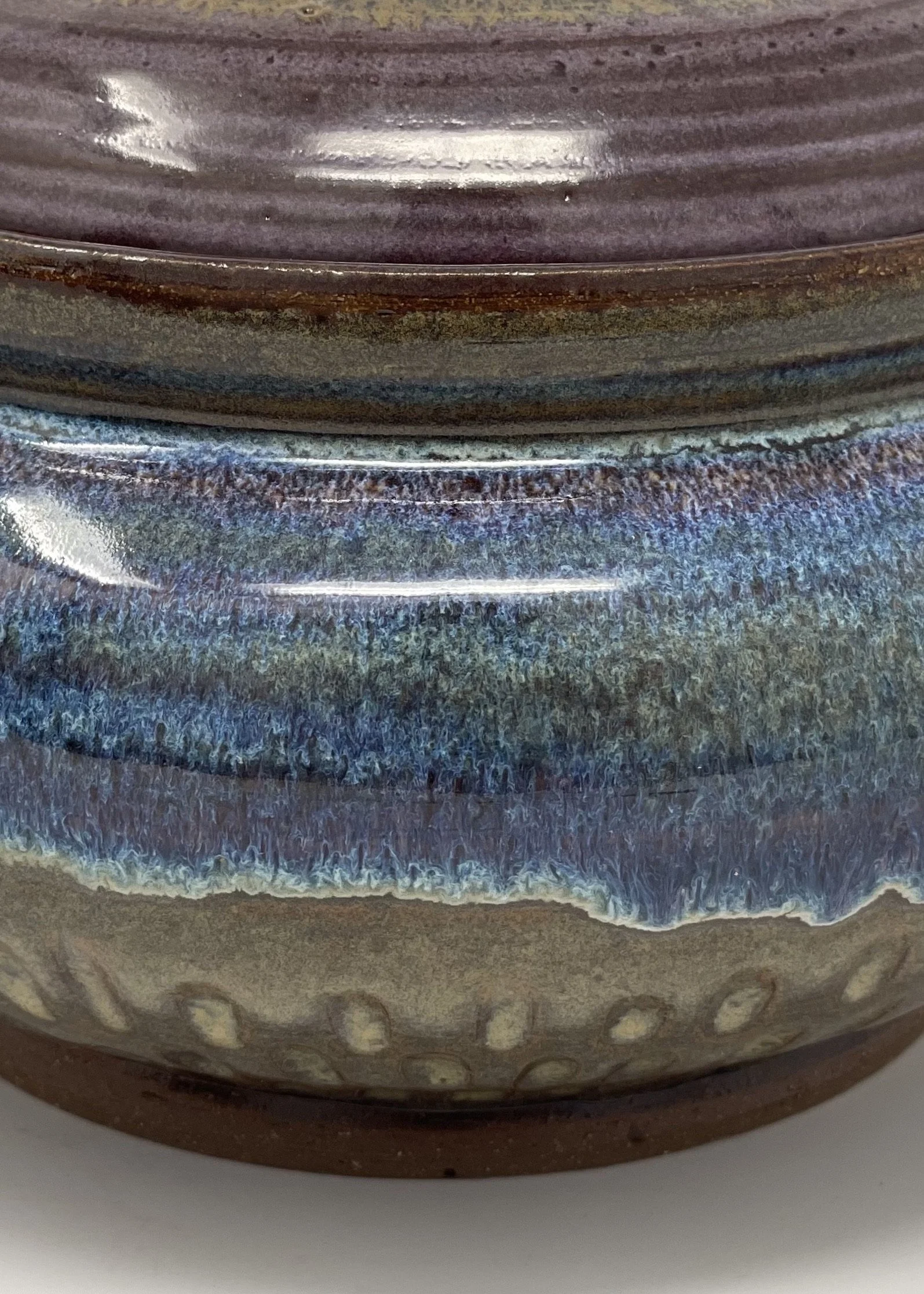 Close-up of a ceramic vase with multicolored glaze in shades of purple, blue, and brown.