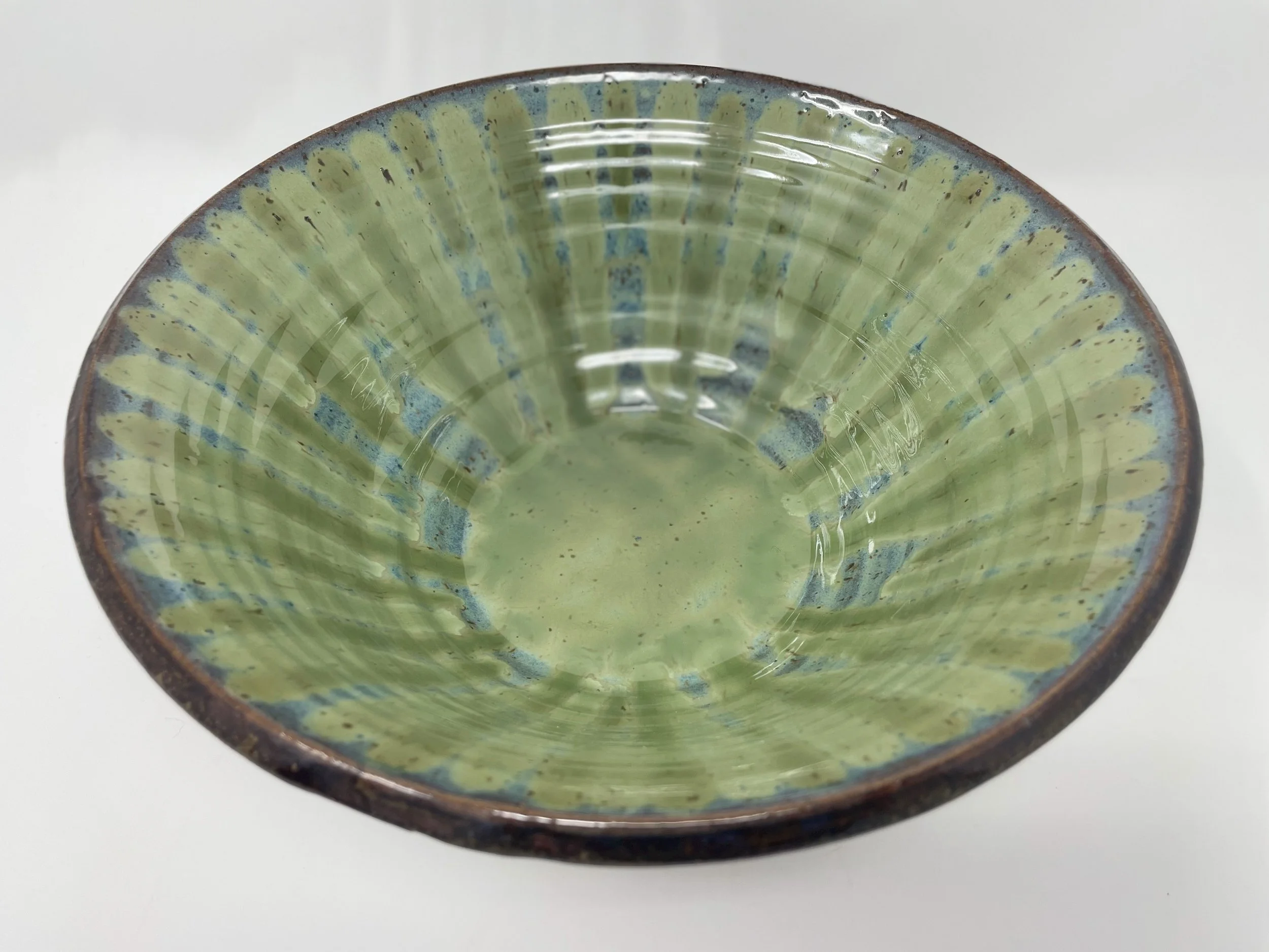 A ceramic bowl with a green glaze and blue accents, viewed from above, on a white surface.