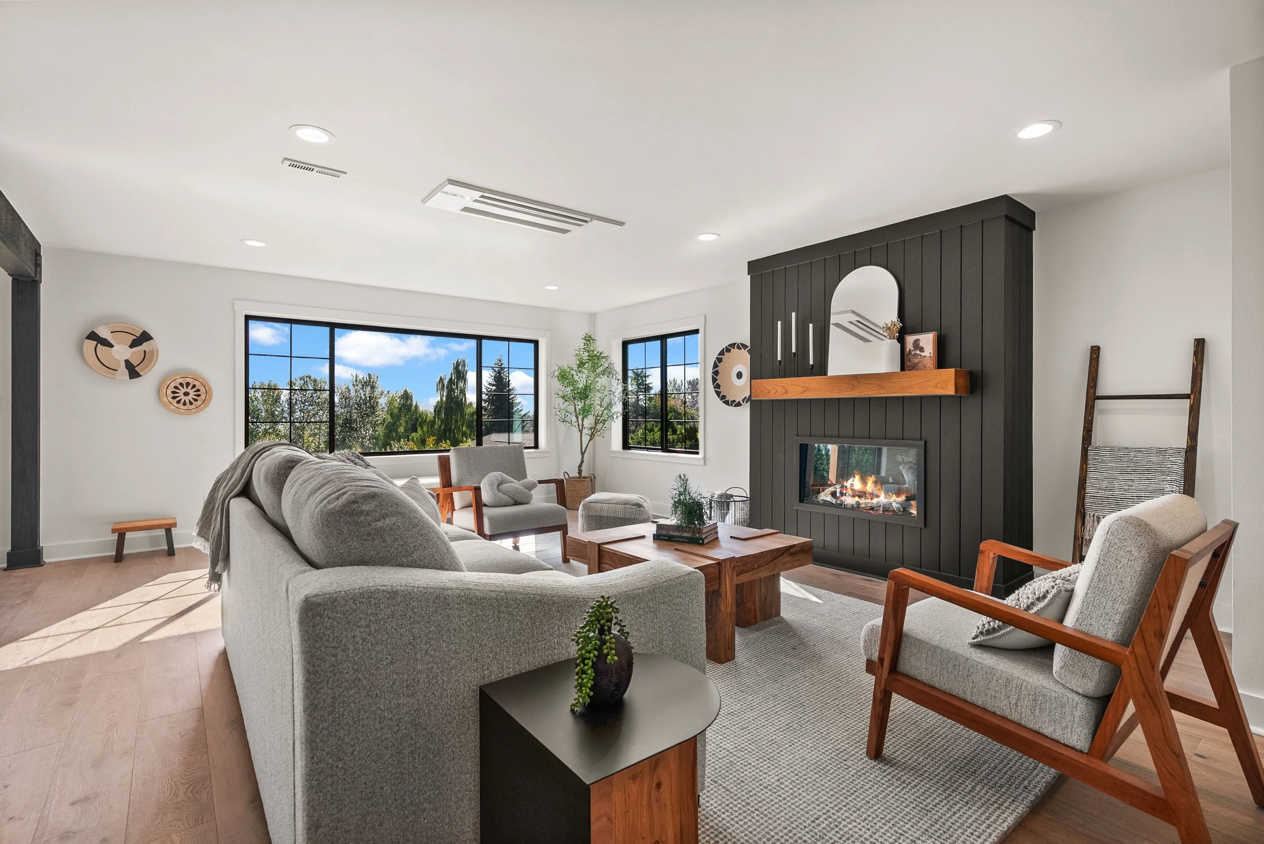 Modern living room with black fireplace feature wall, large picture windows, hardwood floors, and contemporary staging photographed by Spenrol Media.