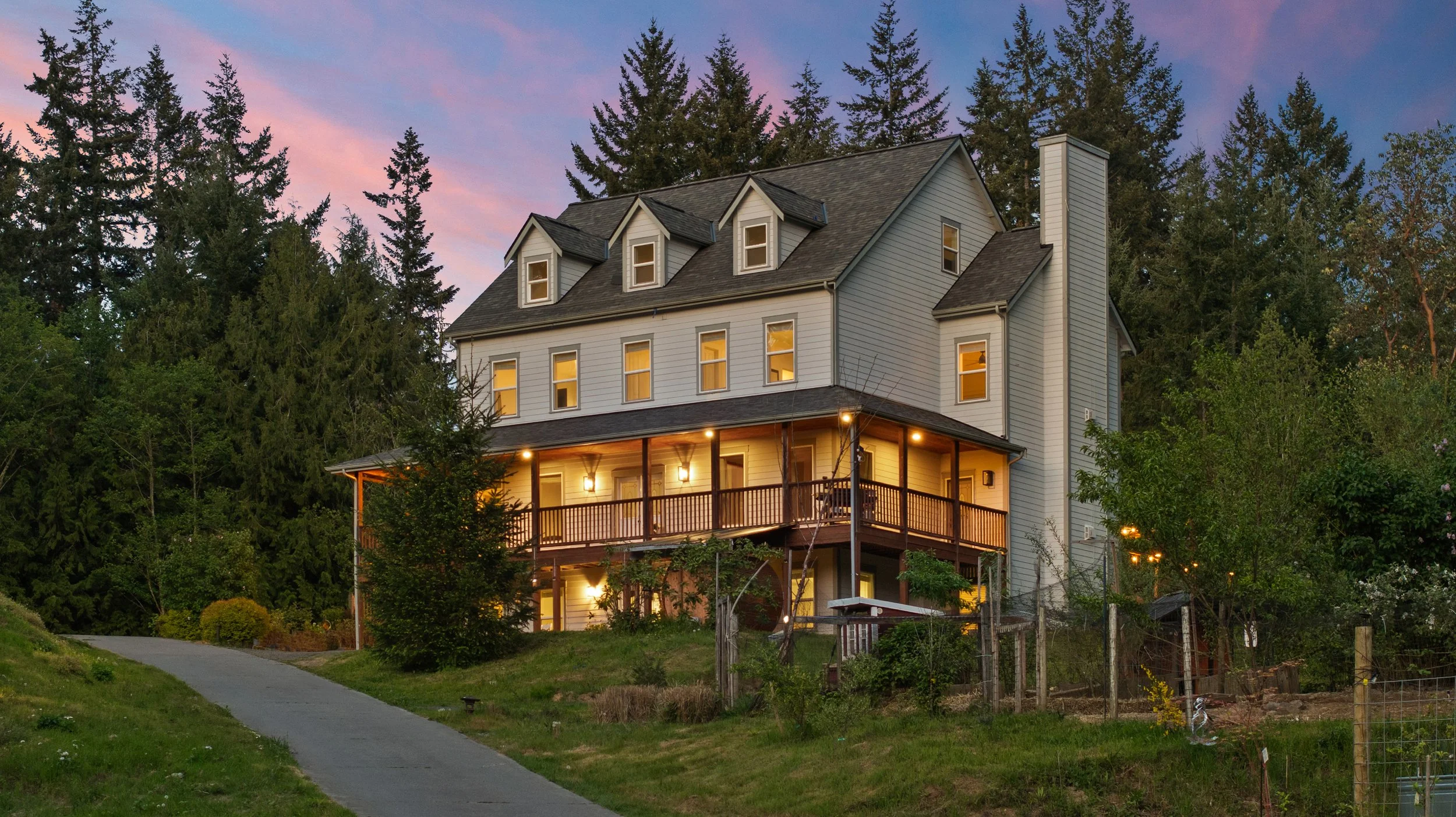 Luxury custom home at sunset with wraparound porch, surrounded by evergreen trees in the Pacific Northwest, photographed by Spenrol Media.