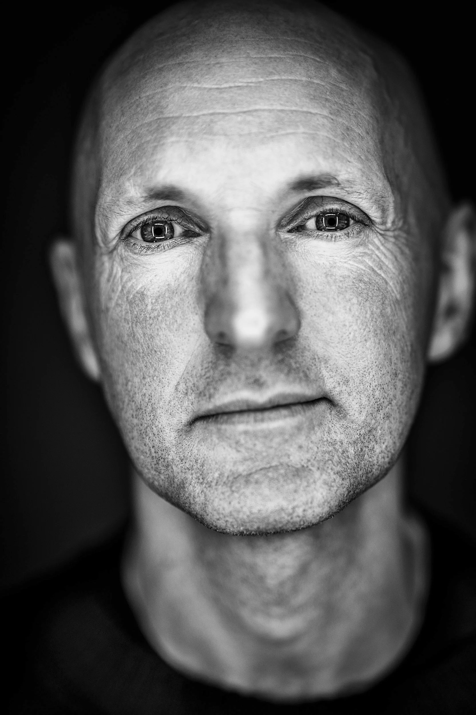 Close-up black and white portrait of a man's face, showing detailed skin texture and intense expression.