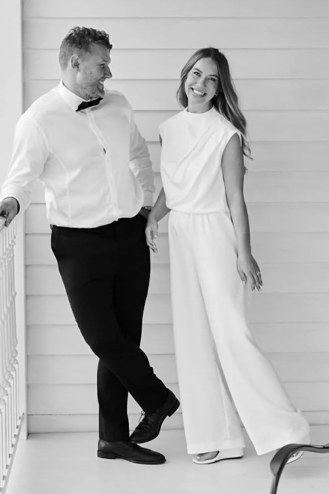 A bride and groom posing for photos.  The bride wears a white bodice and wide leg pants