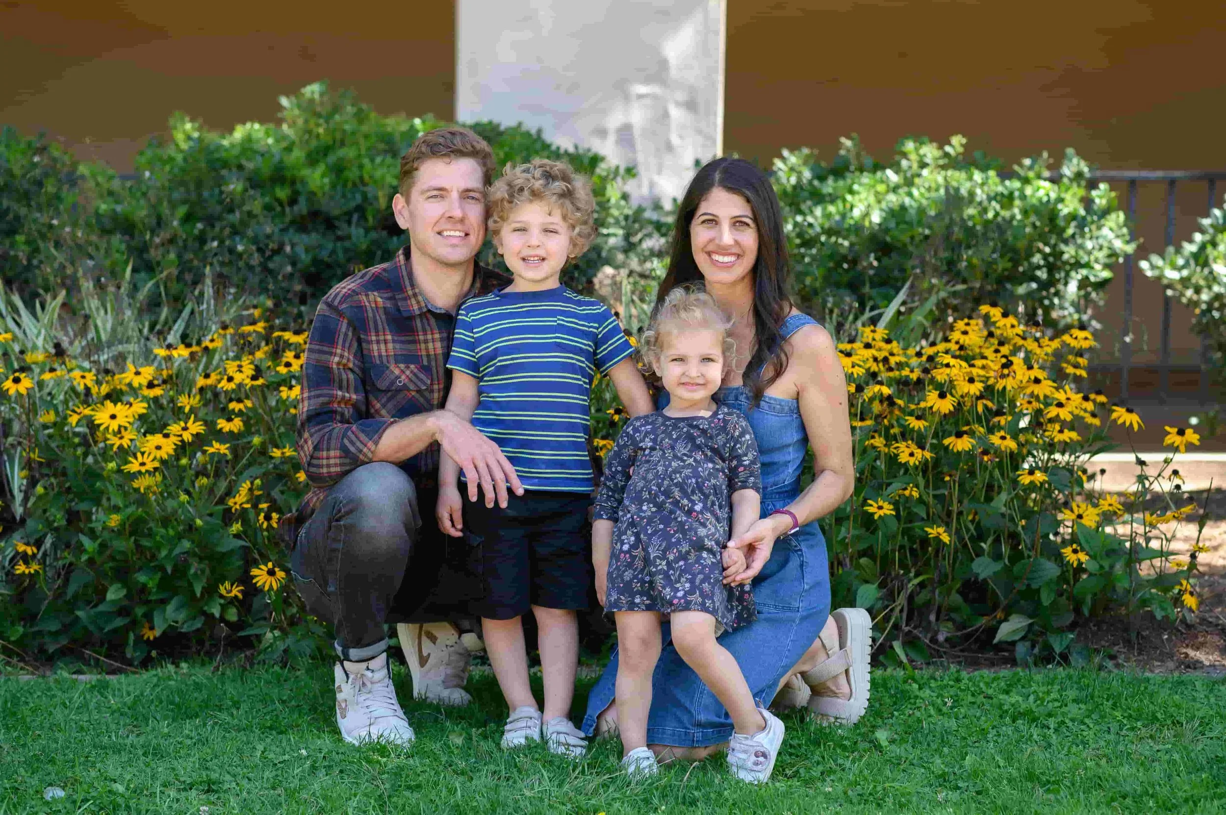 Young parents kneeling with two children in front of garden